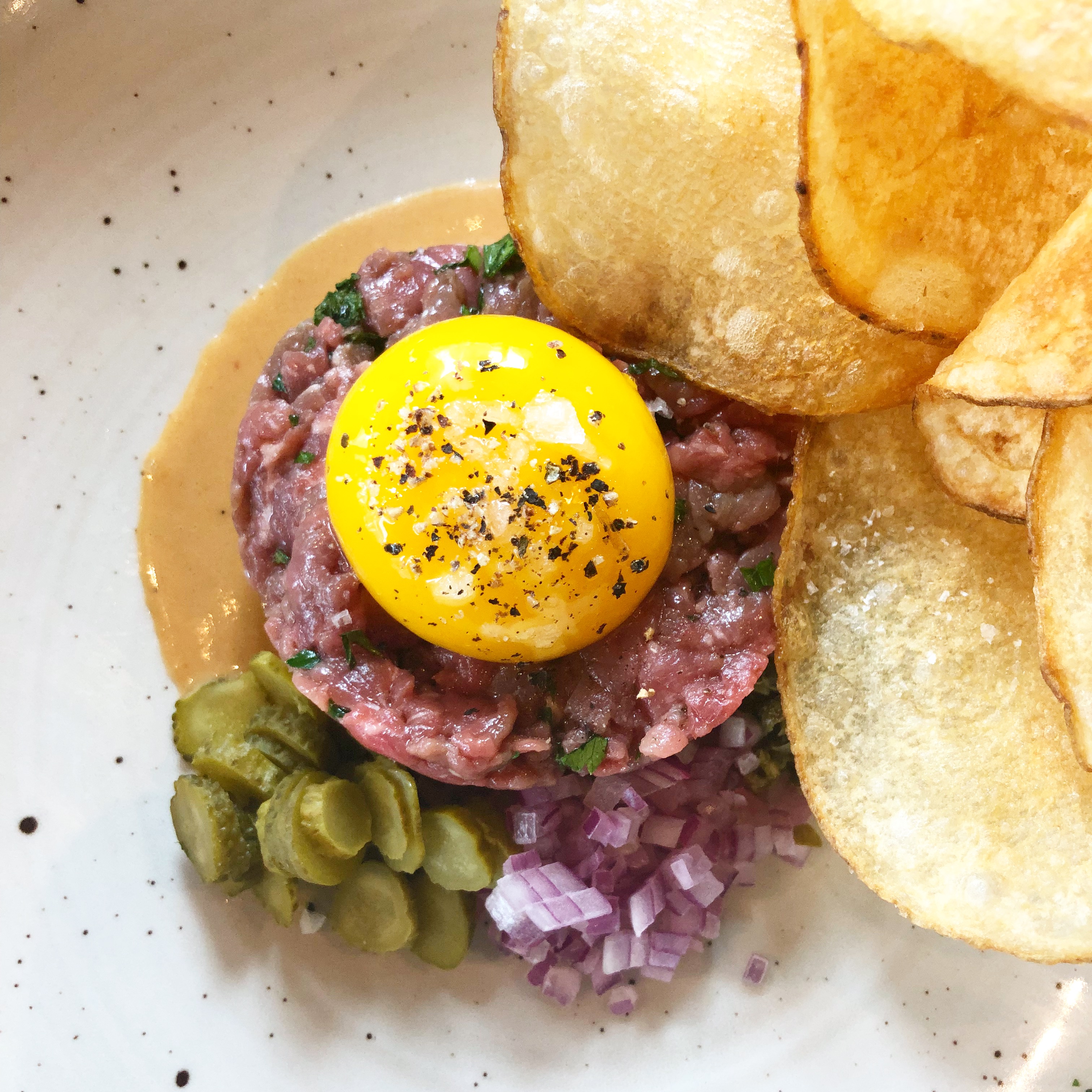 Steak tartare is topped with a fat yellow yolk, with cornichons and chips, at Bistro Agnes.