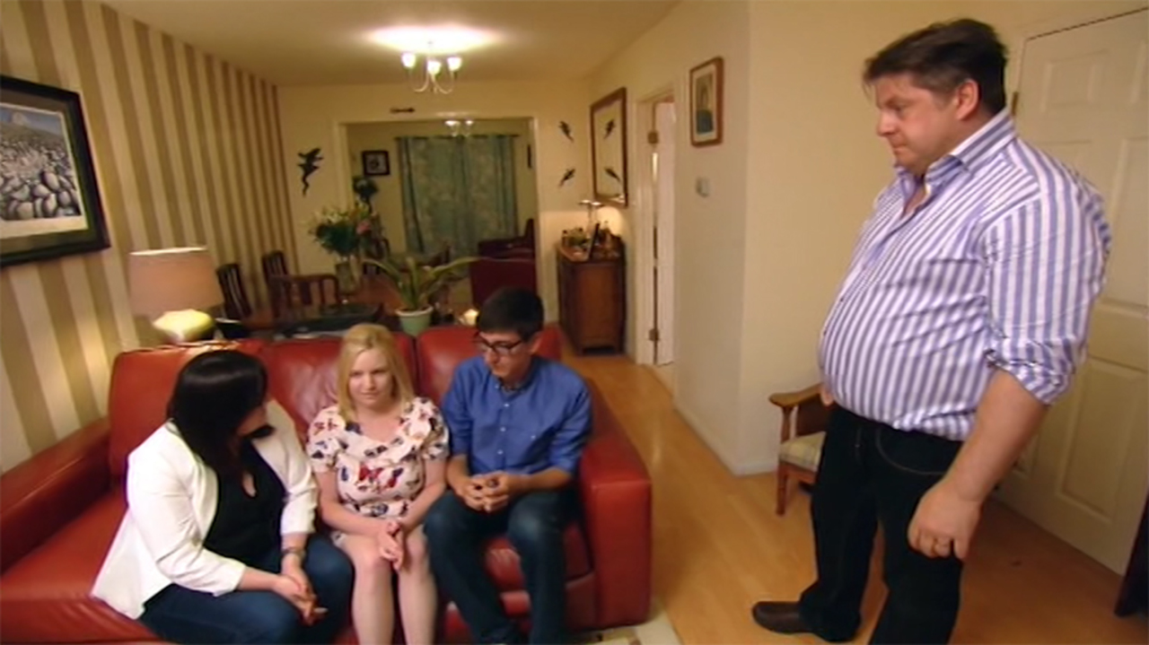 Three Come Dine With Me contestants — two women and one man — sit on a red sofa, while a fourth, a man, stands to their right looming angrily over them.