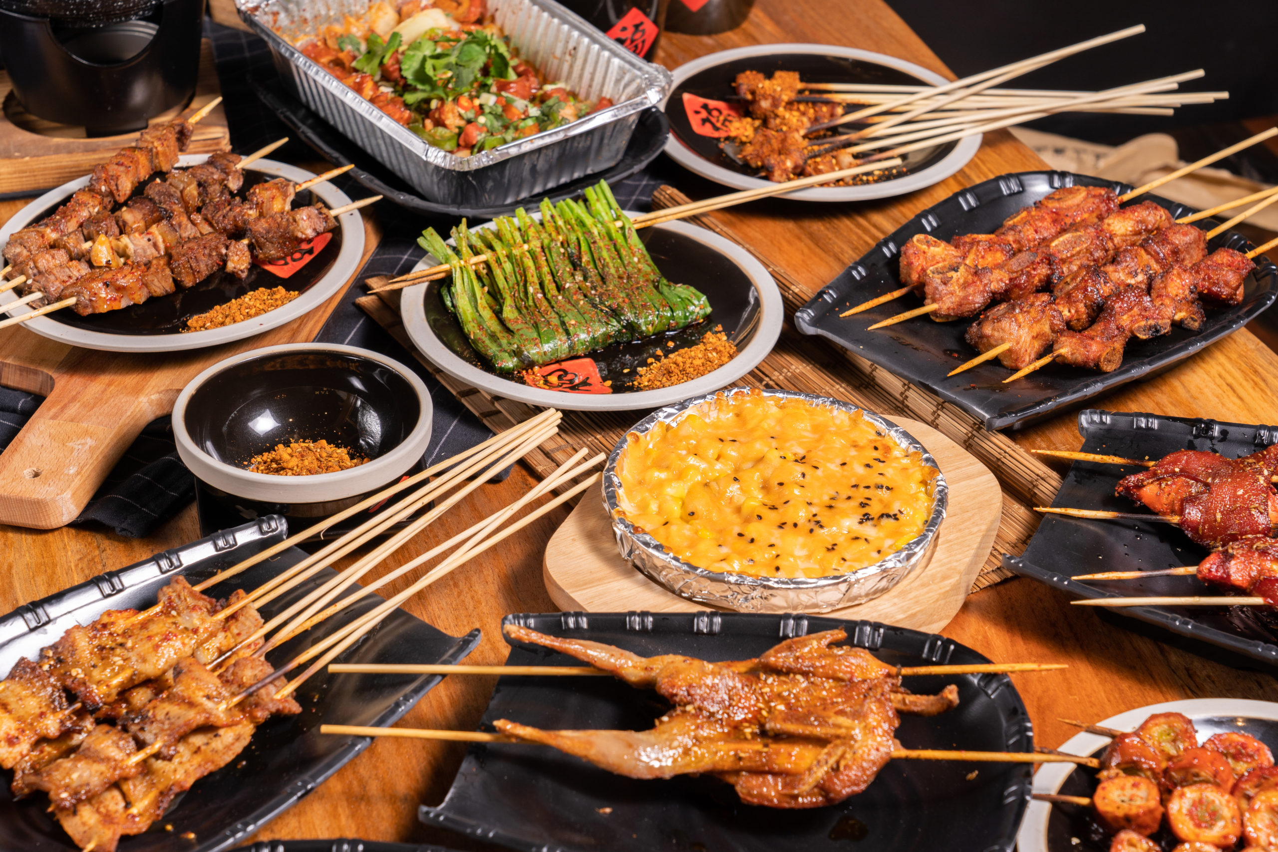 A table full of plates of various skewers, including meat, shrimp, and vegetables