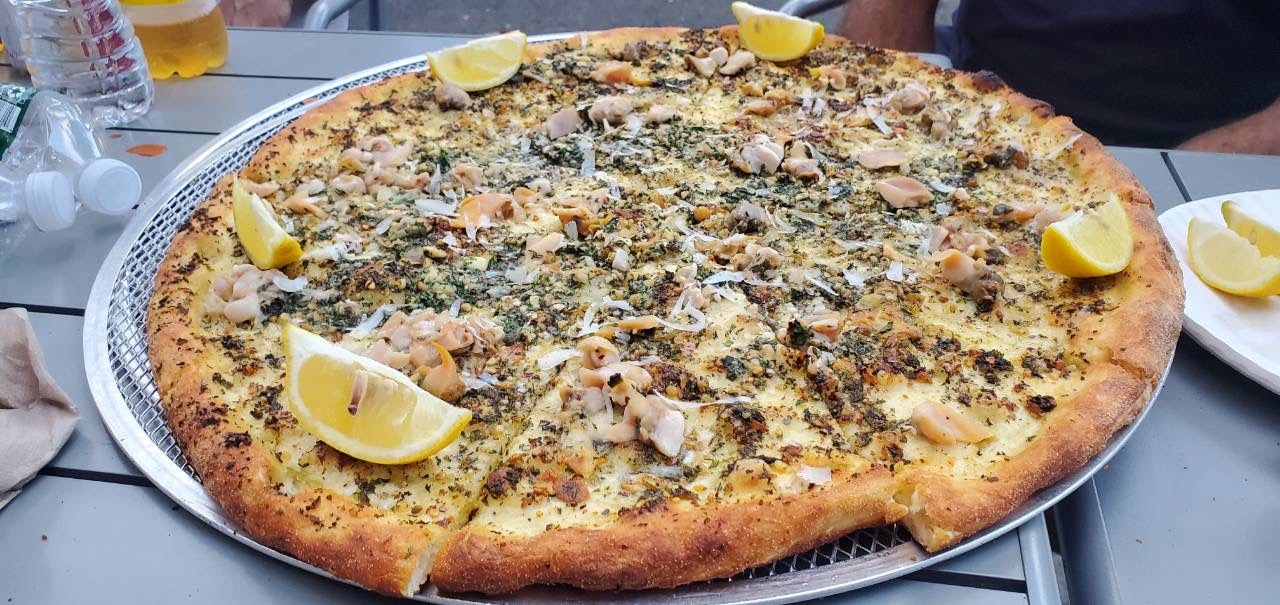 A close-up photo of a clam pizza with lemon wedges set around the outer rim.