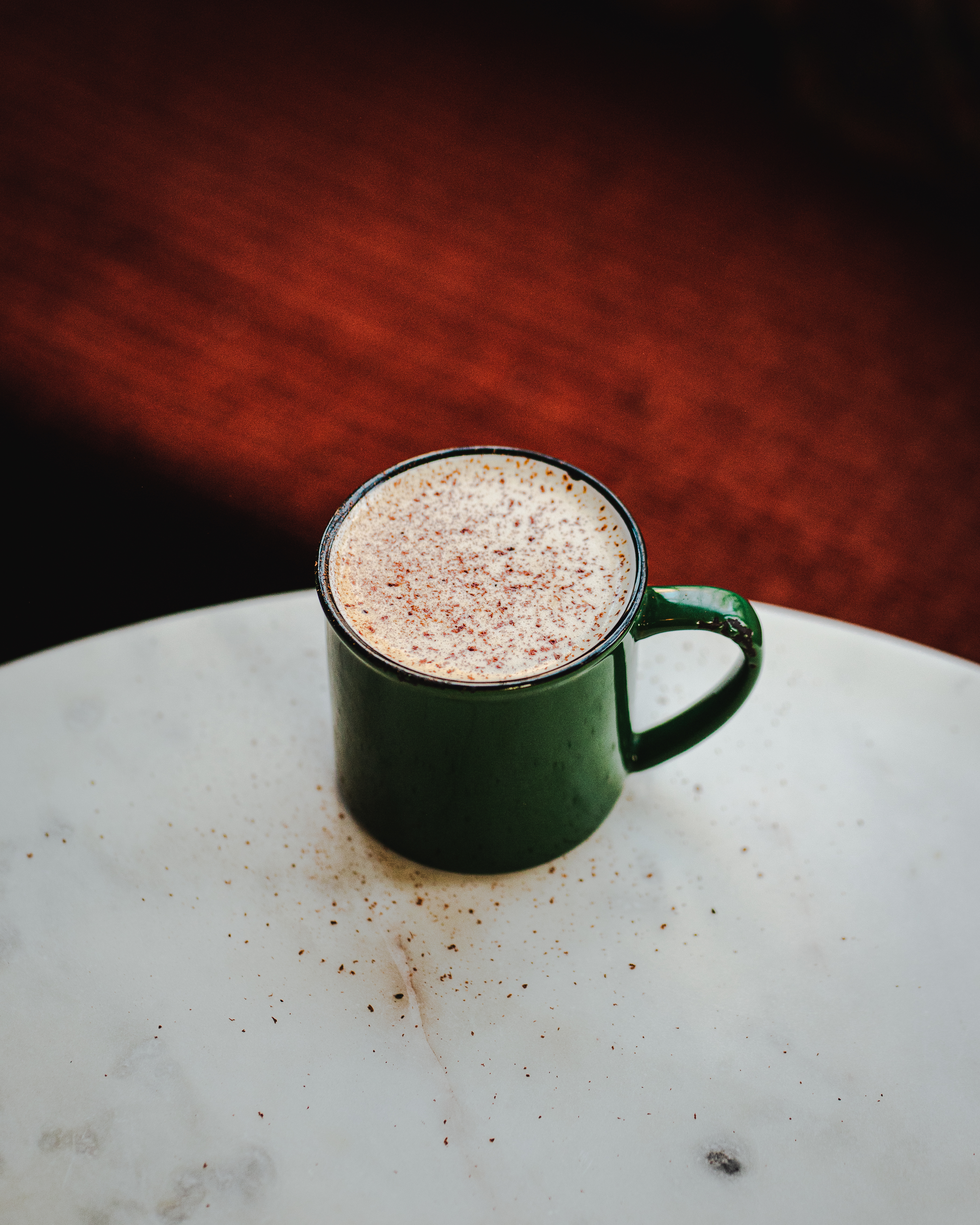 A shiny green mug filled with frothy spiked chai, placed on a marble table.