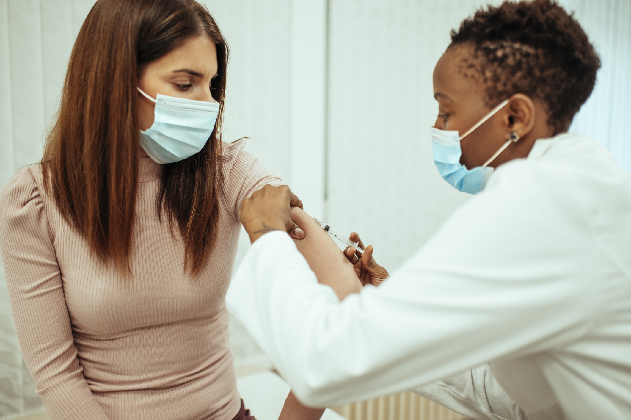 A doctor administers a vaccine to a patient. Both  are wearing blue face masks.