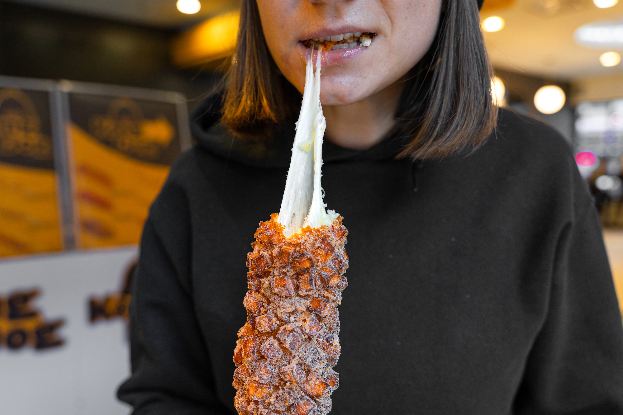 A woman pulls a string of cheese from a hot dog coated batter, sweet potato, and deep fried.