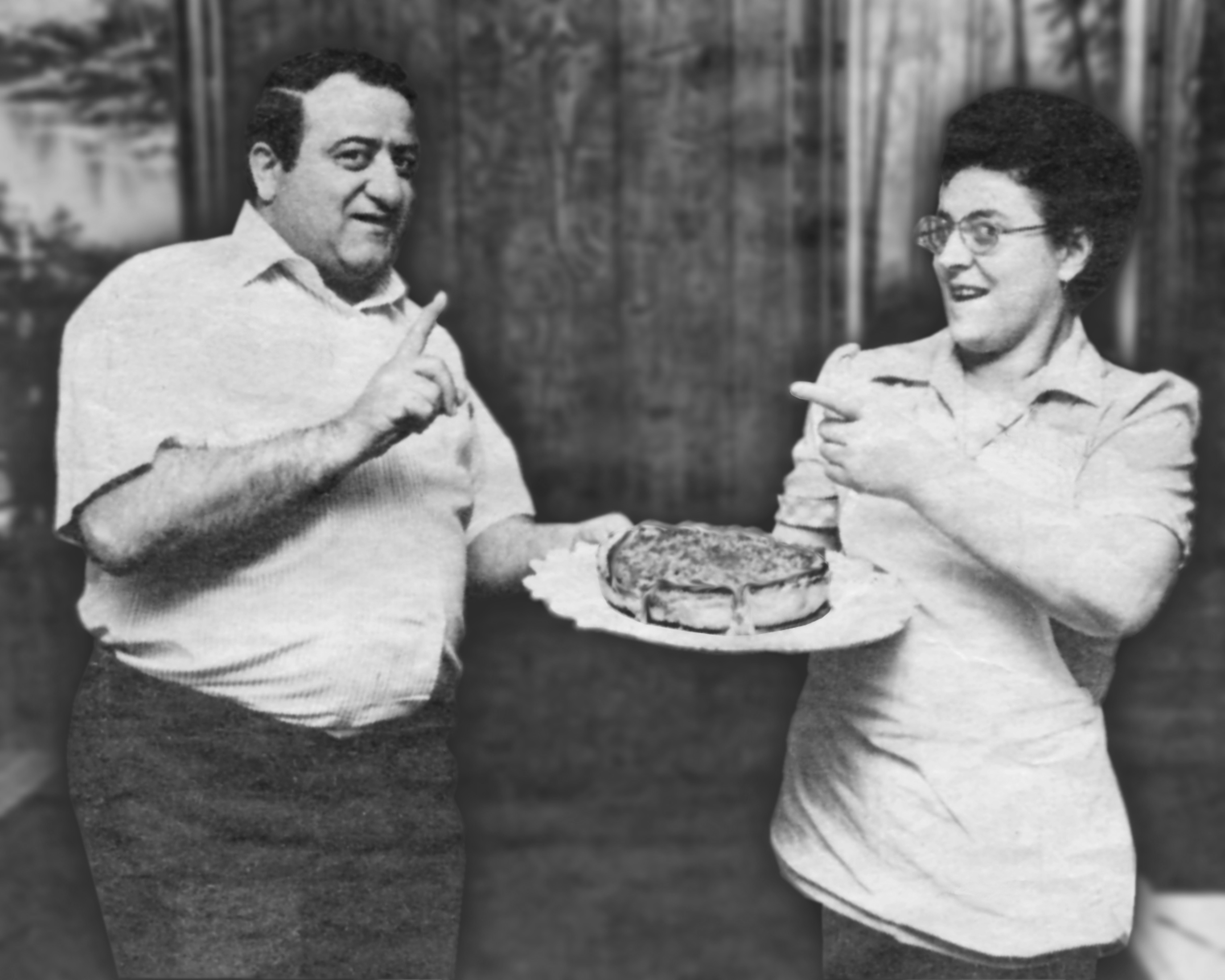A man and a woman carry a plate containing a stuffed pizza and point at each other
