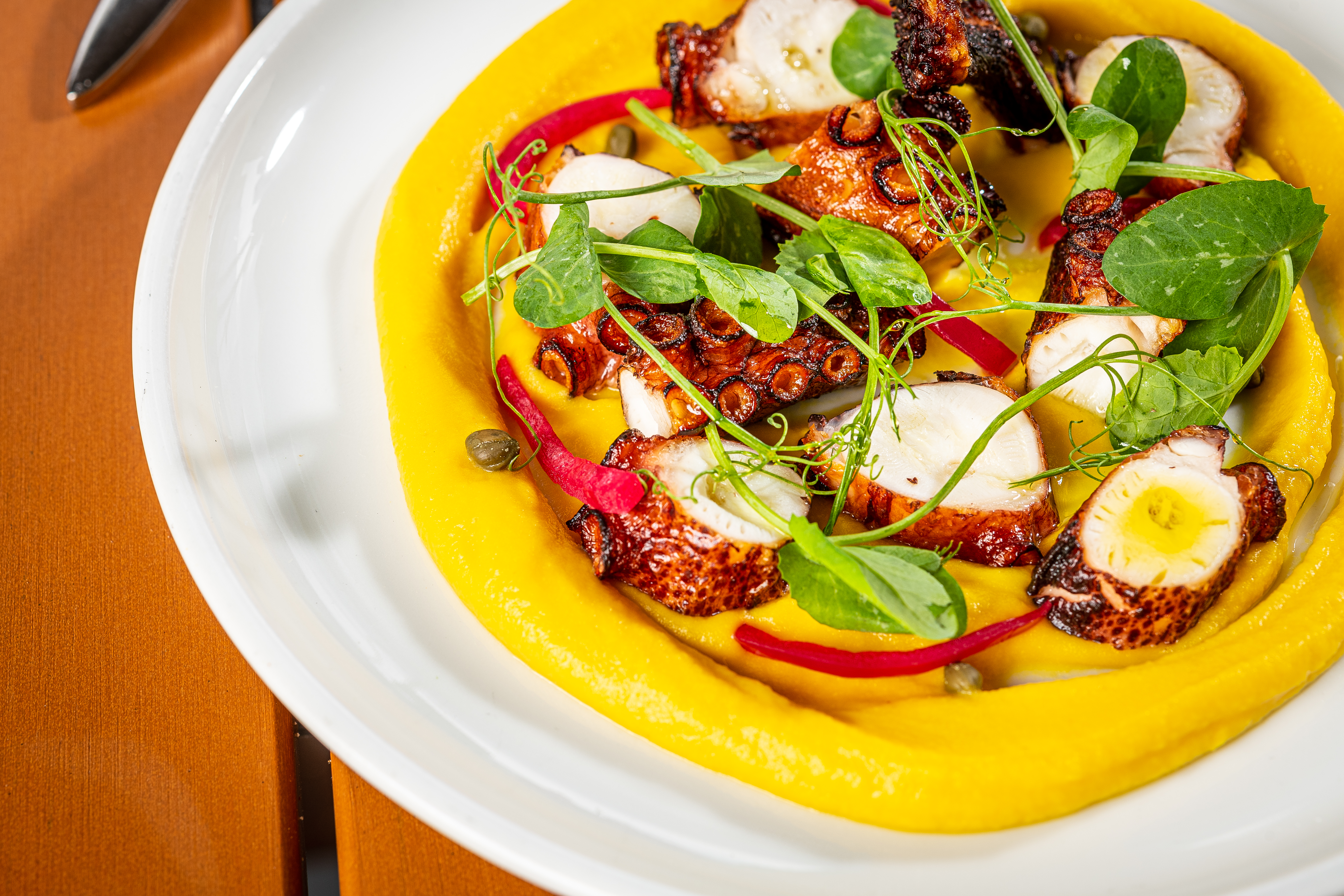 Slices of octopus are scattered in a vibrant yellow sauce with greens.