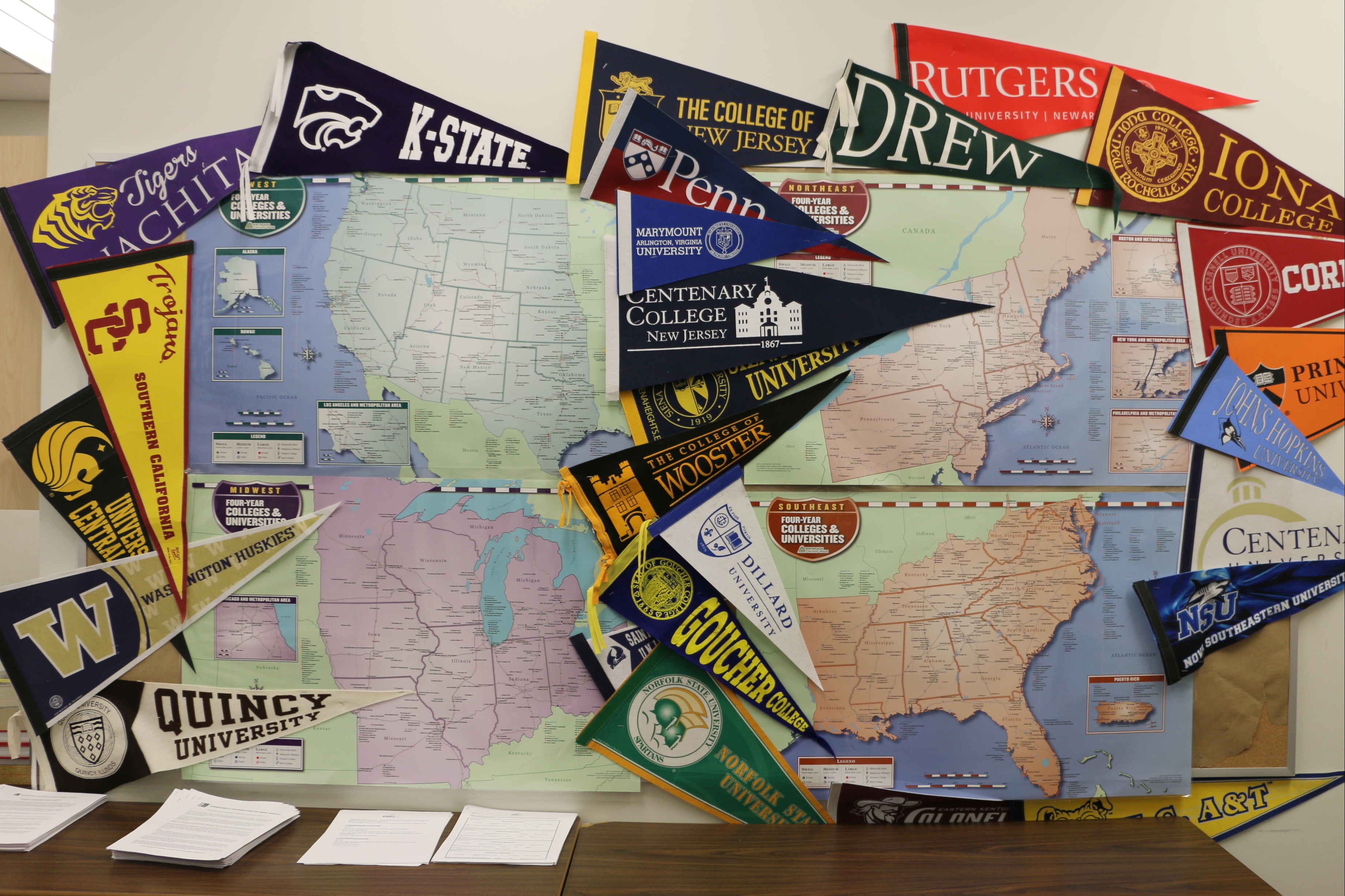 A wall is decorated with college pennants surrounding maps of different parts of the United States.