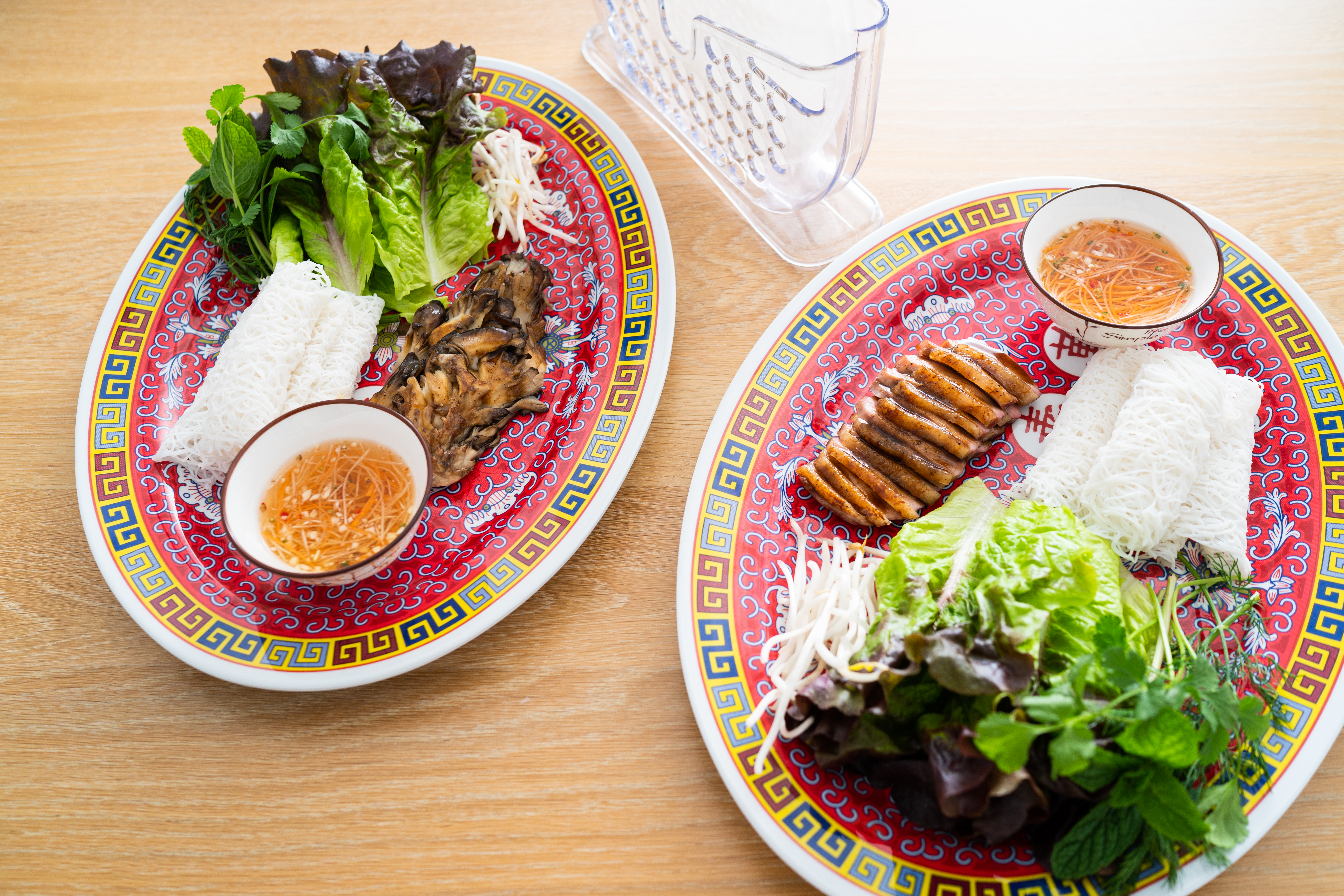 Two plates of rice papers, lettuces, herbs, and lan-roc pork on matching plates.