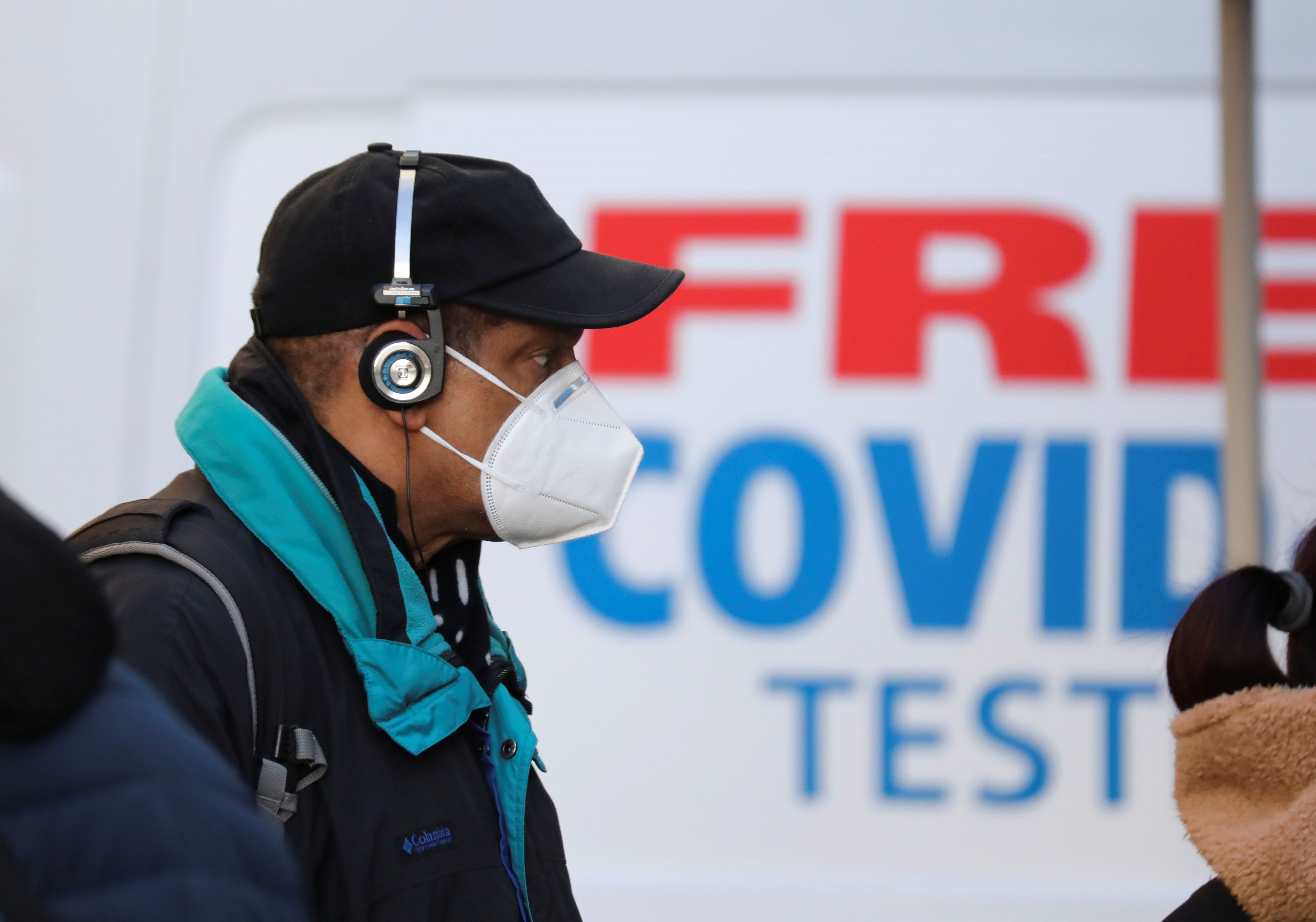 A person wearing an N95 face mask walking past a sign that reads “free covid tests.”
