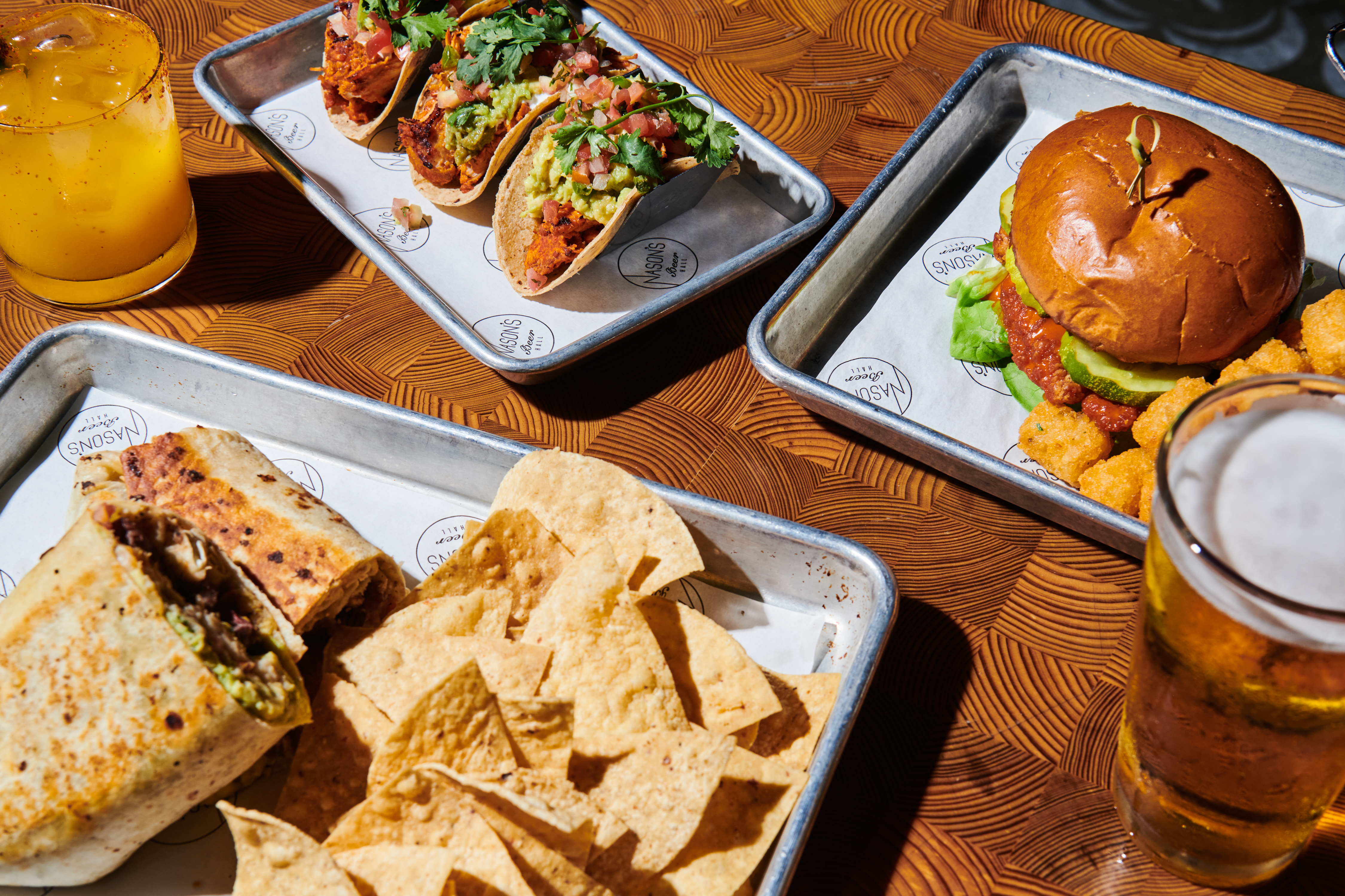 Tacos, a burger, burrito, and beer on a table.