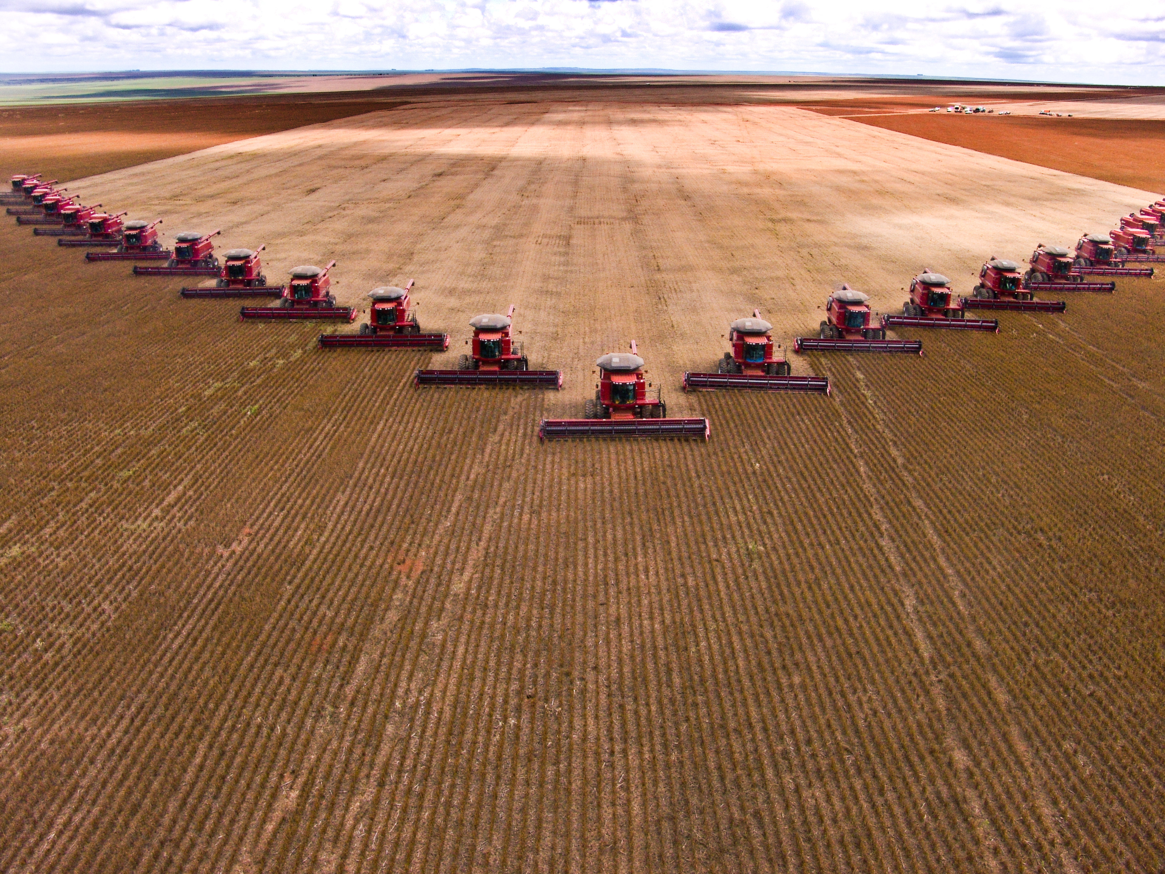 Two dozen tractors drive in a triangular pattern across a huge field.