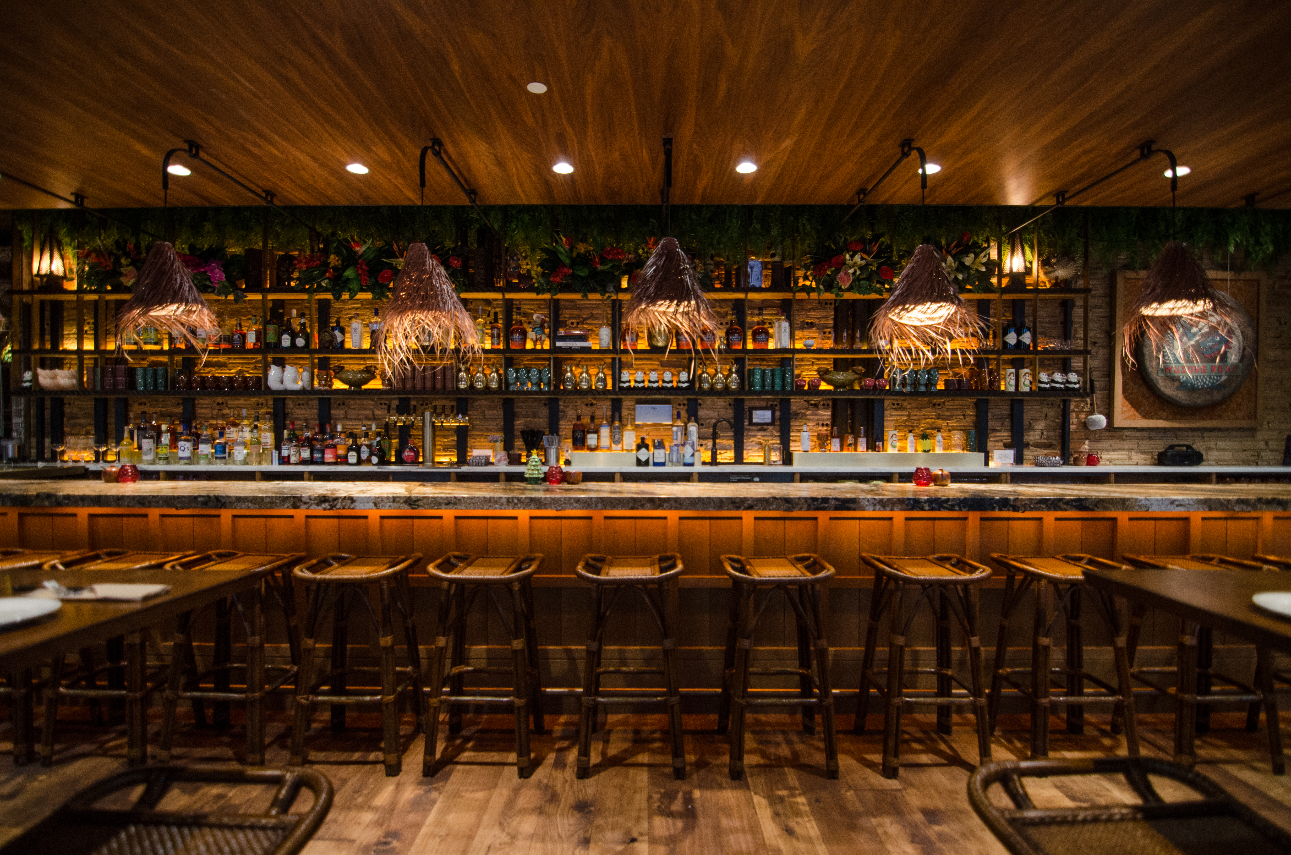 一个tiki酒吧的看法与篮子灯，五颜六色的玻璃器皿和一个锣与餐馆名称，乌古路，绘了它。