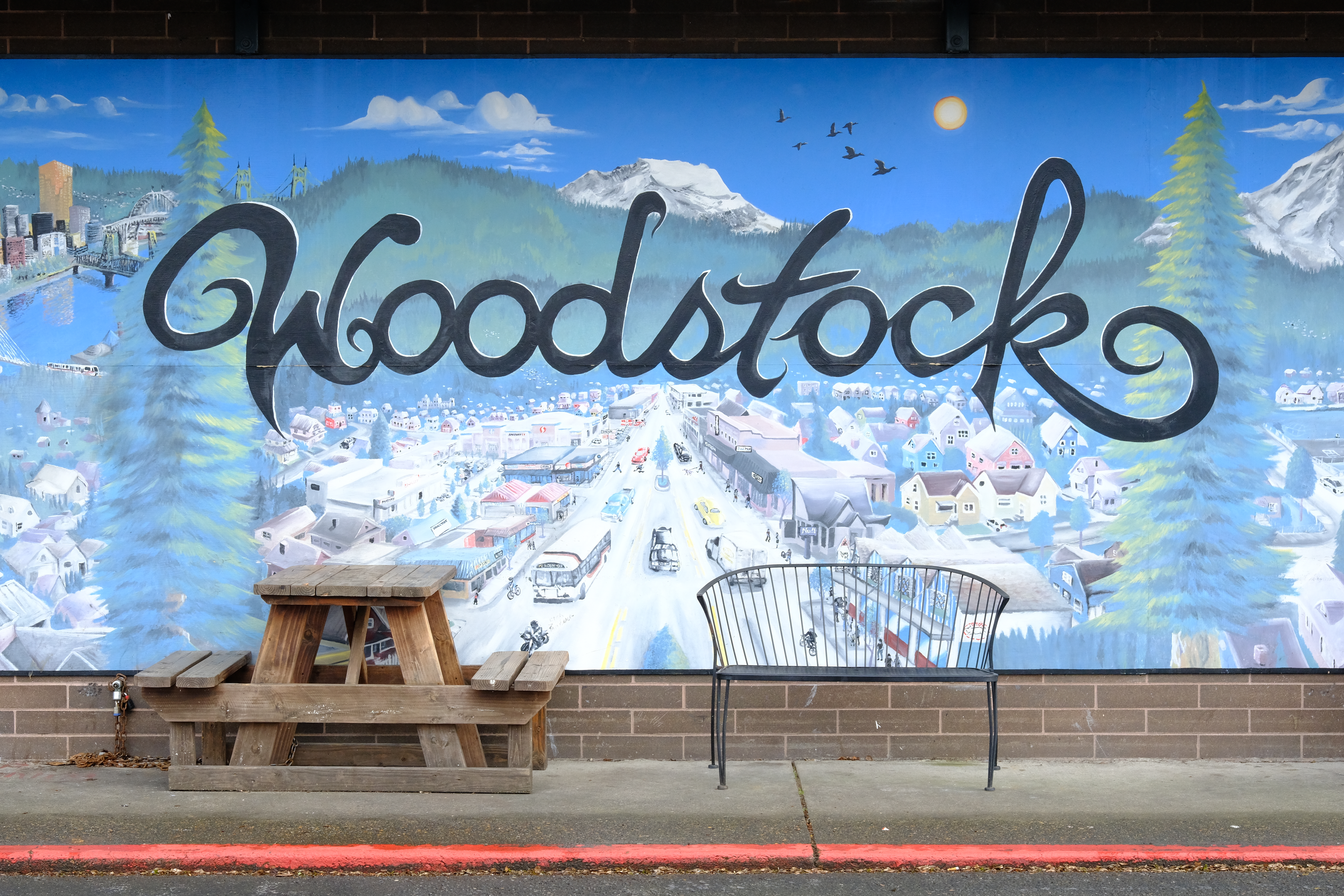 Mural of the Woodstock neighborhood in front of a picnic table and park bench