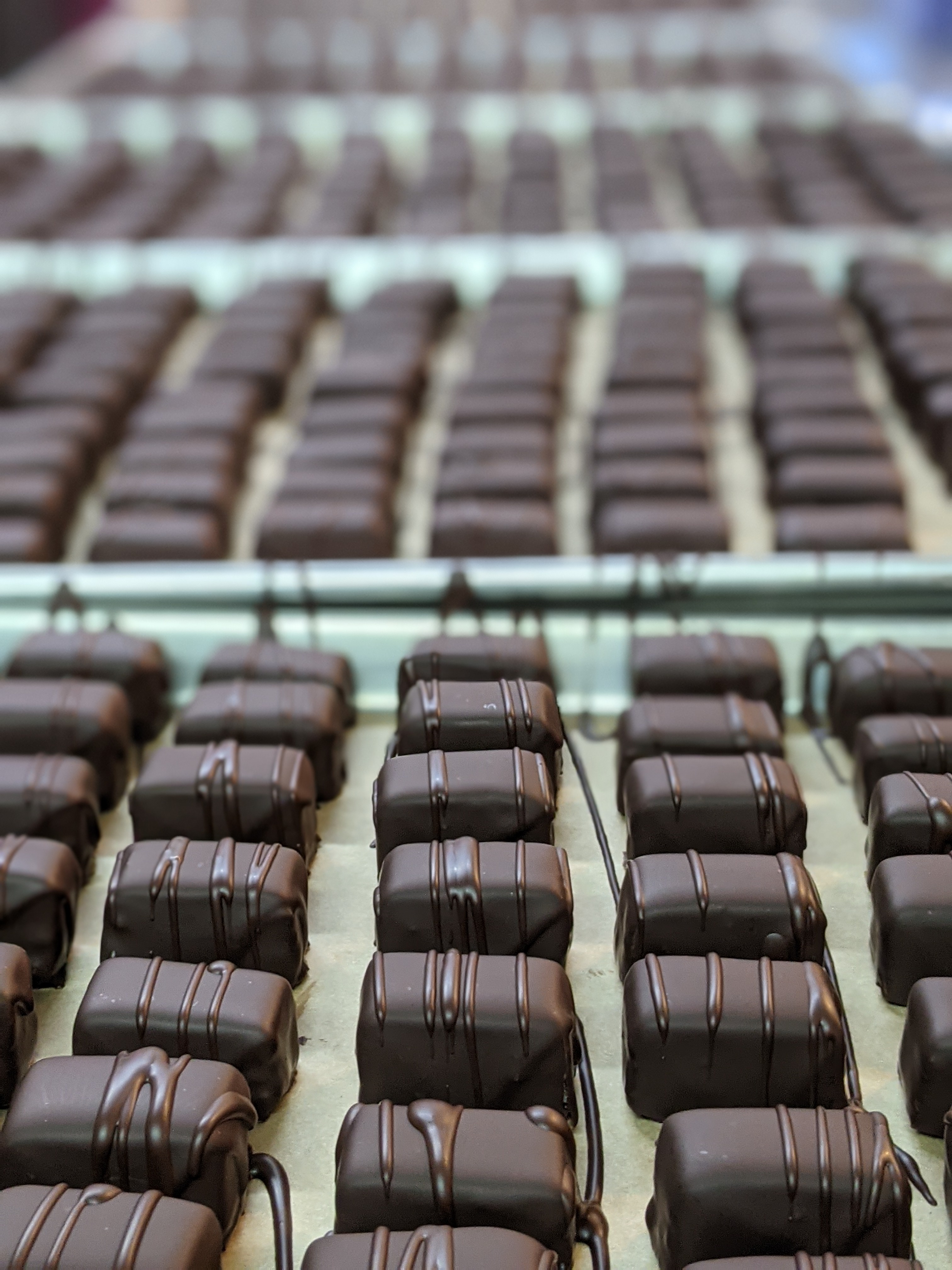 Multiple rows of chocolates on parchment paper in an assembly line.