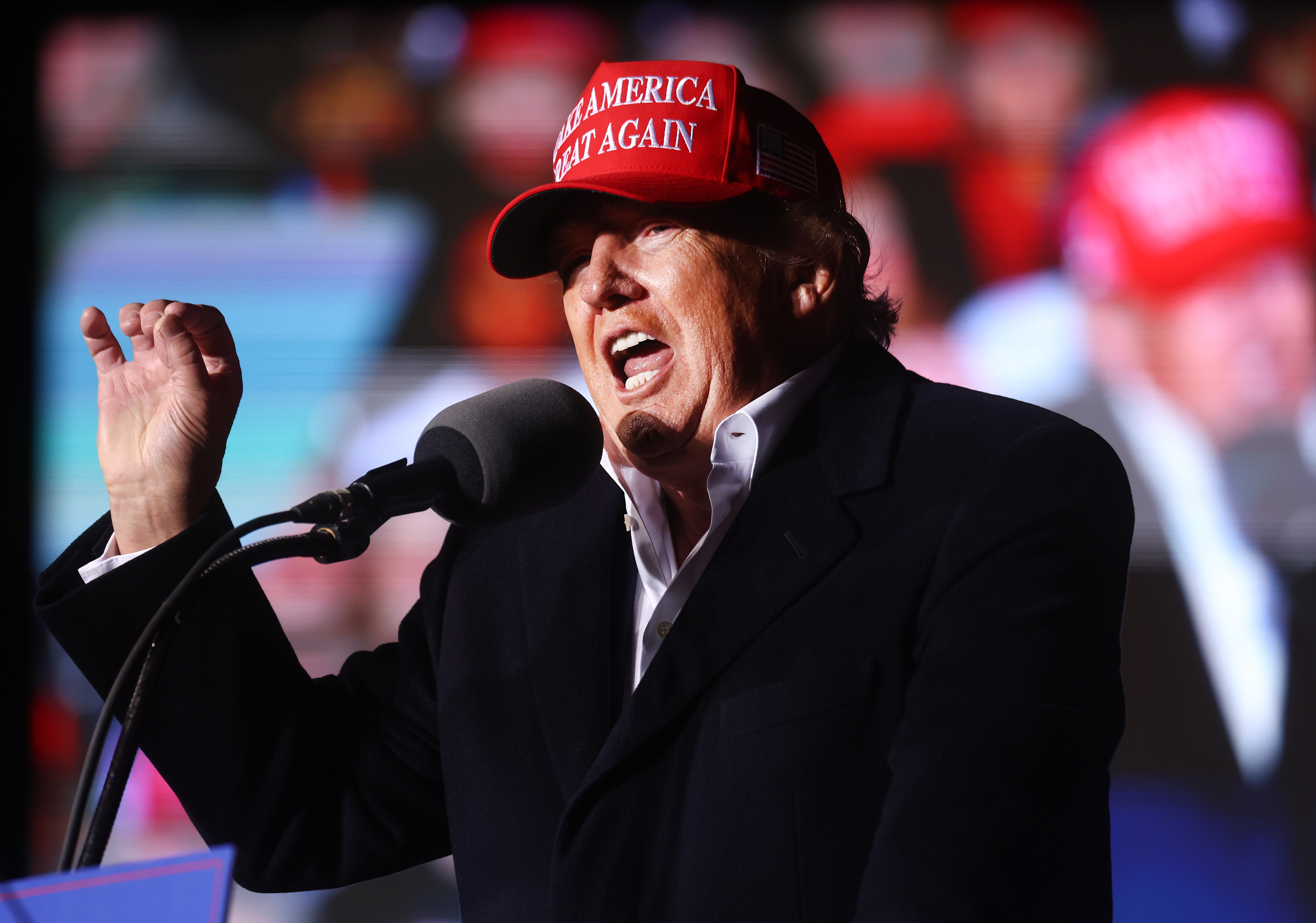 Former President Donald Trump, wearing a red Make America Great Again hat, gestures from behind a microphone on stage at a rally in Florence, Arizona, on January 15, 2022.