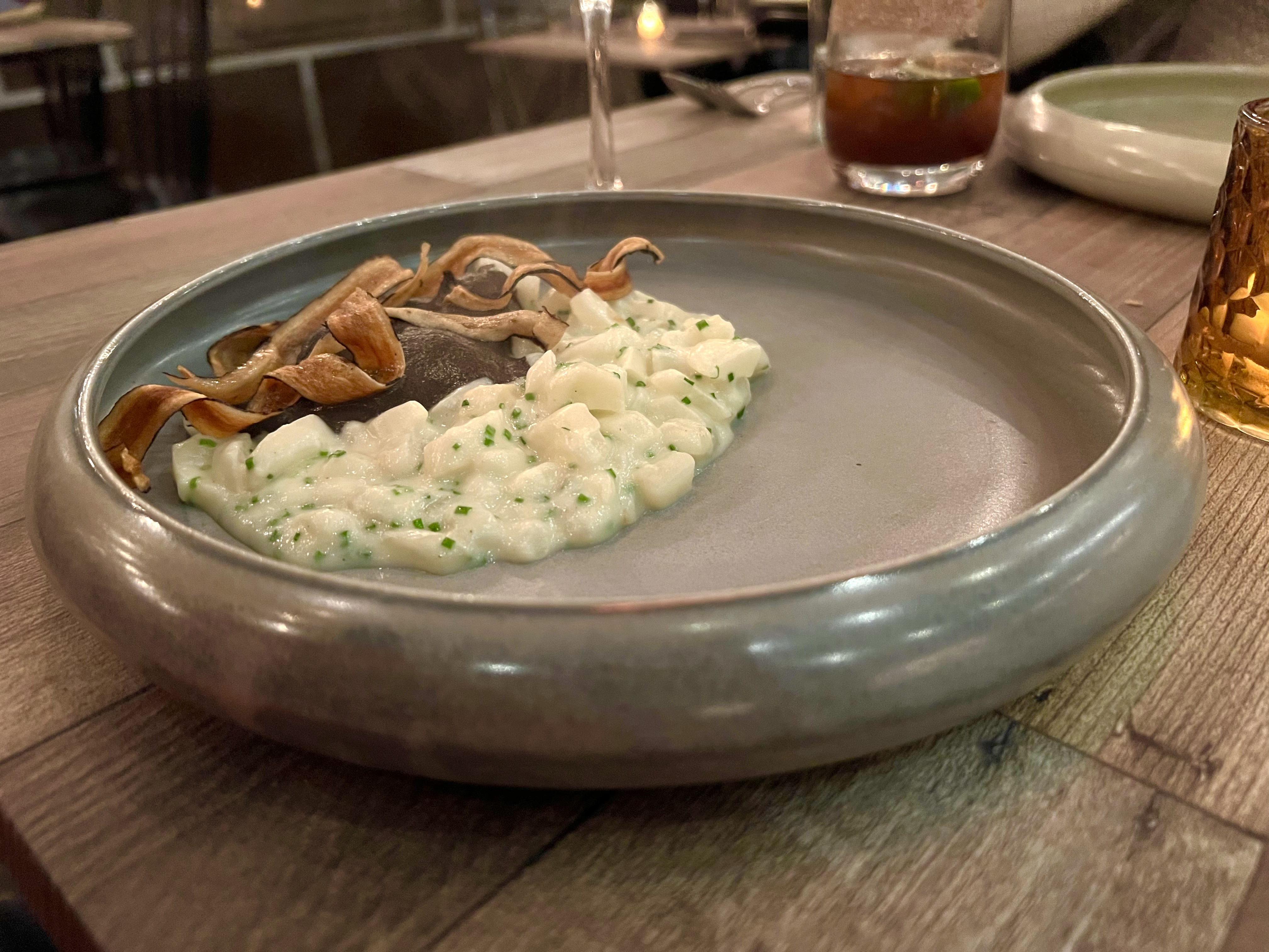 A pile of salsify risotto sits at the far edge of an empty grey bowl, next to grey trumpet mushroom puree