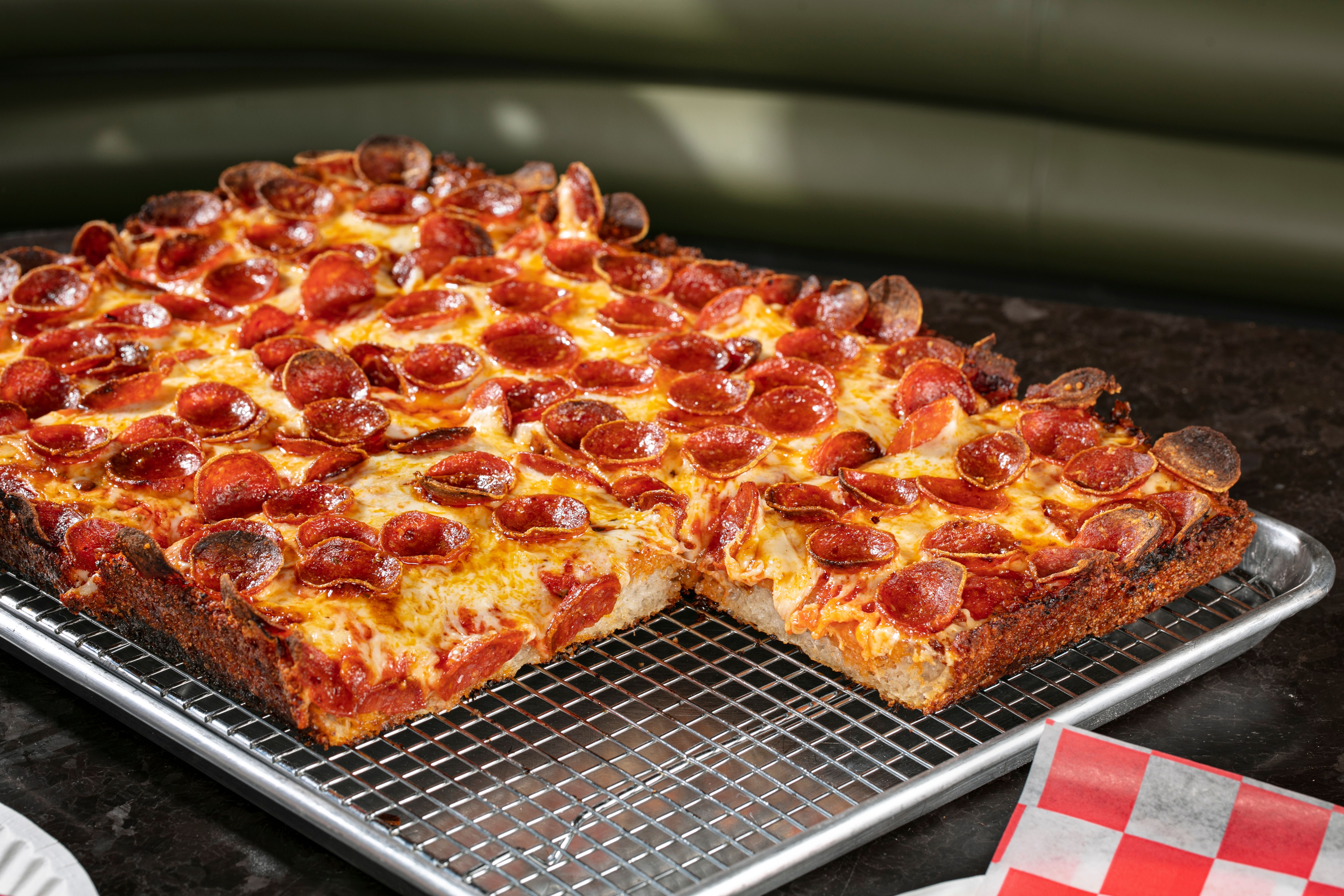 A photo of a square, thick pepperoni pie covered in cheese and roni cups cooling on a metal grate.