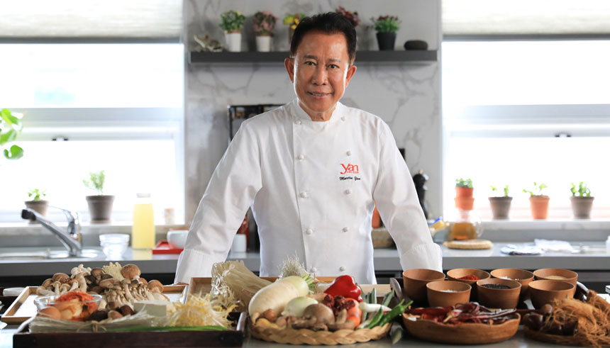 A man in a white chef’s coat stands in front of a counter with food on it. 