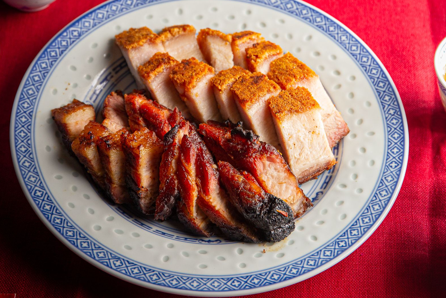 Char siu and siu yuk from Three Uncles on a white and blue plate, on top of a red tablecloth