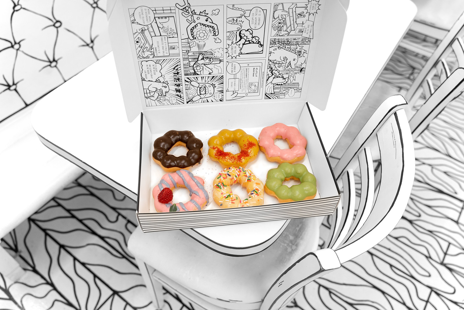 Six colorful mochi doughnuts inside a black and white box.