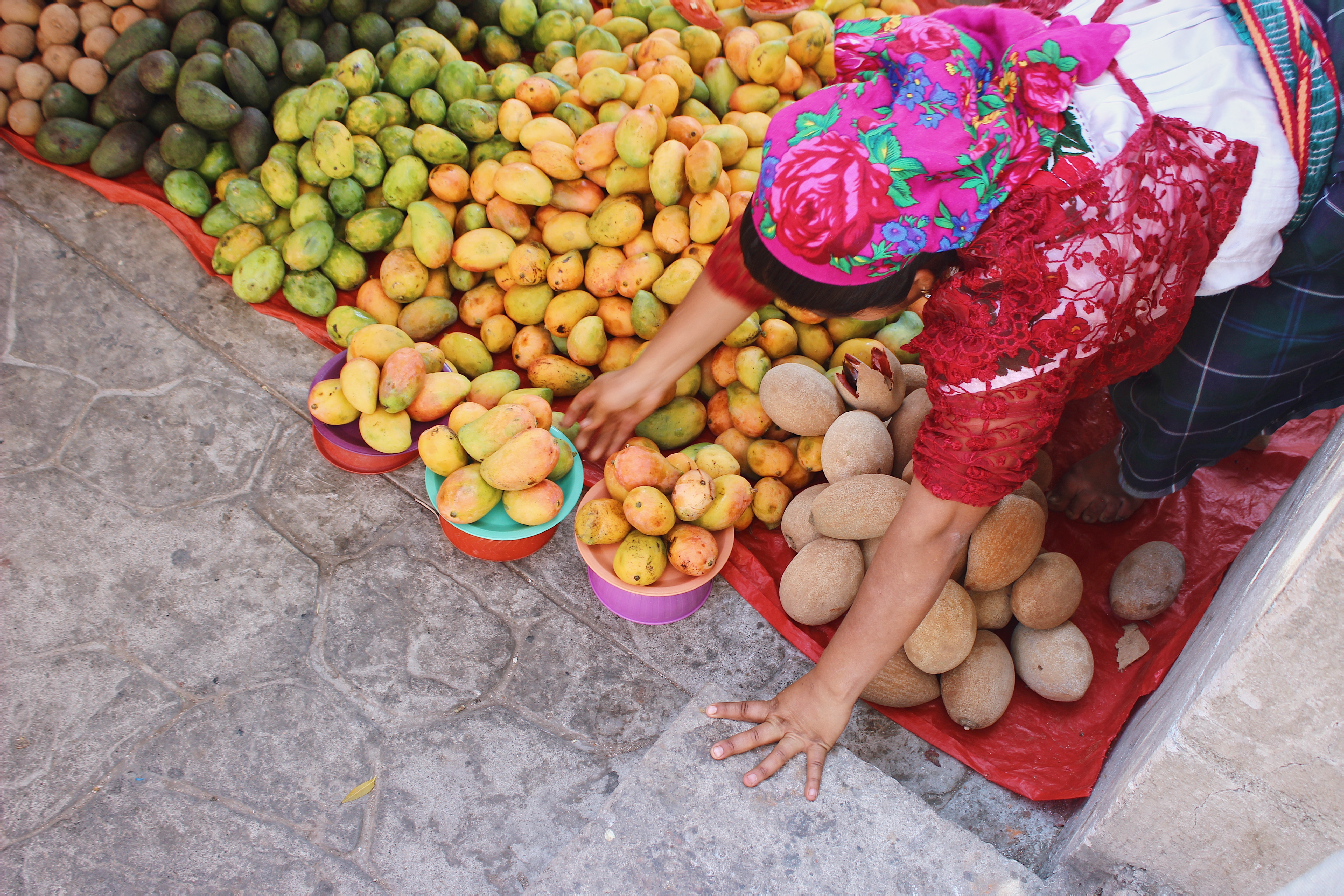 Woman wearing traditional dress sets out different varieties of mangoes on a blanket.