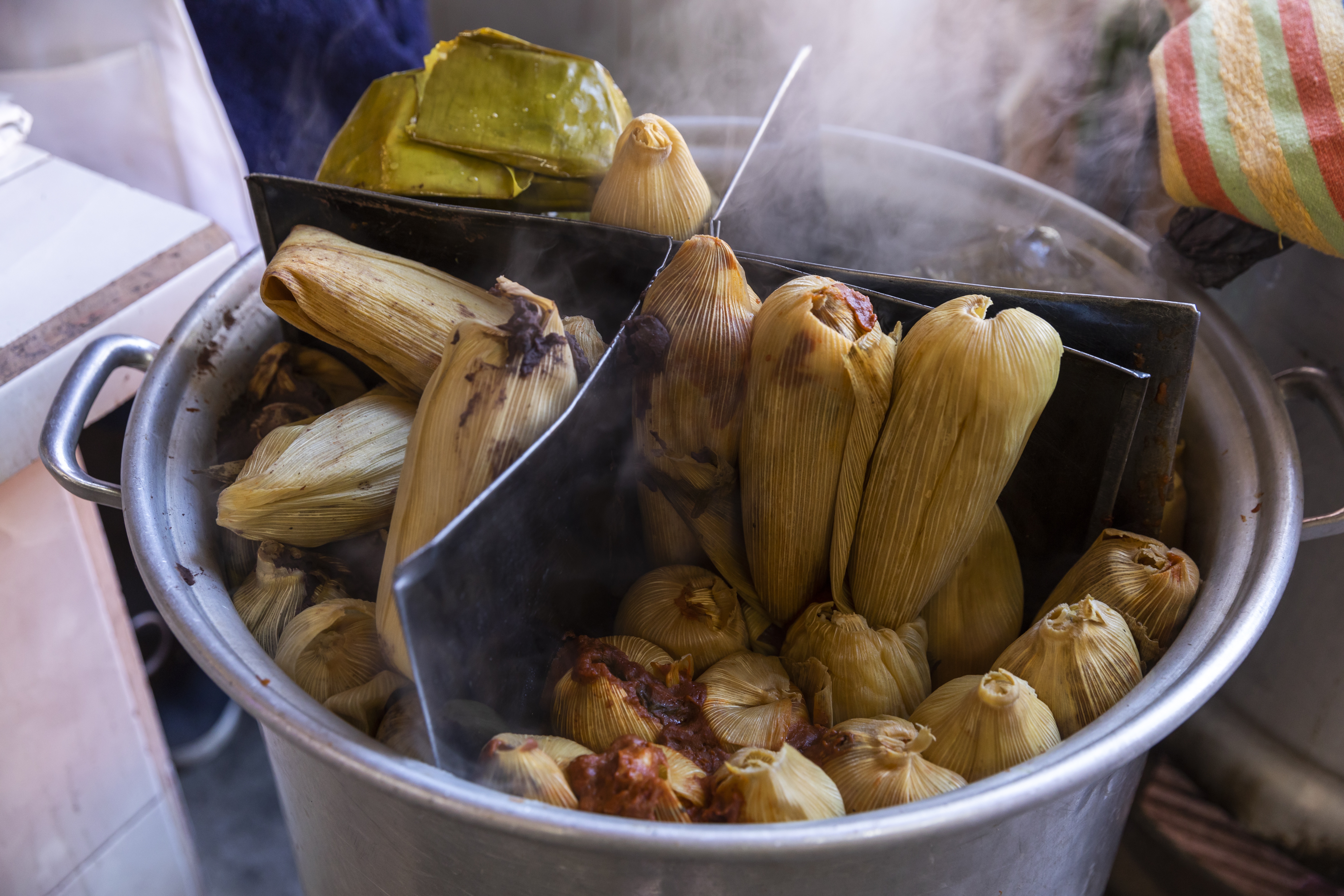 Large steamer pot divided into four sections with different styles of tamales in each.