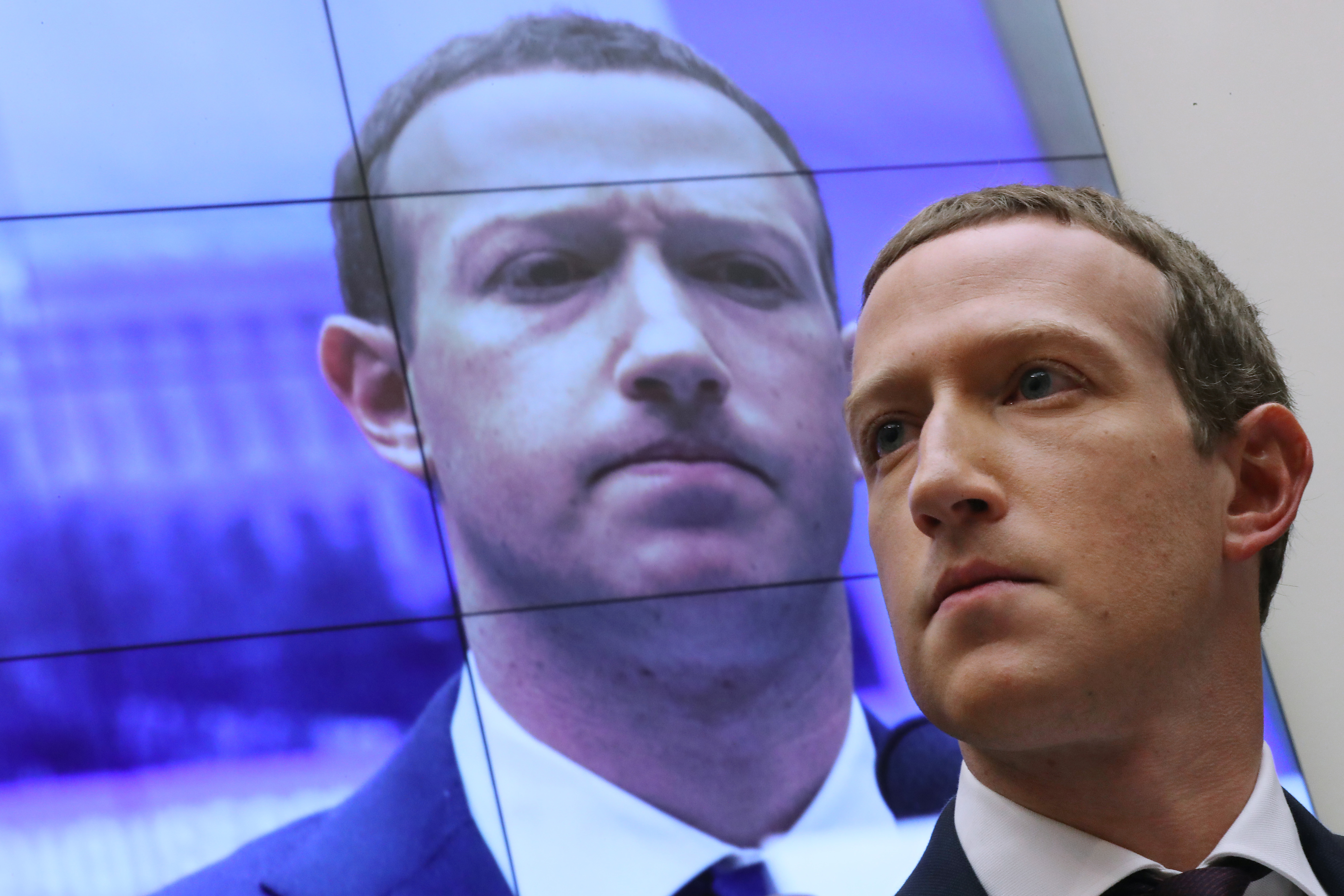 Mark Zuckerberg’s face appearing on a screen behind him.