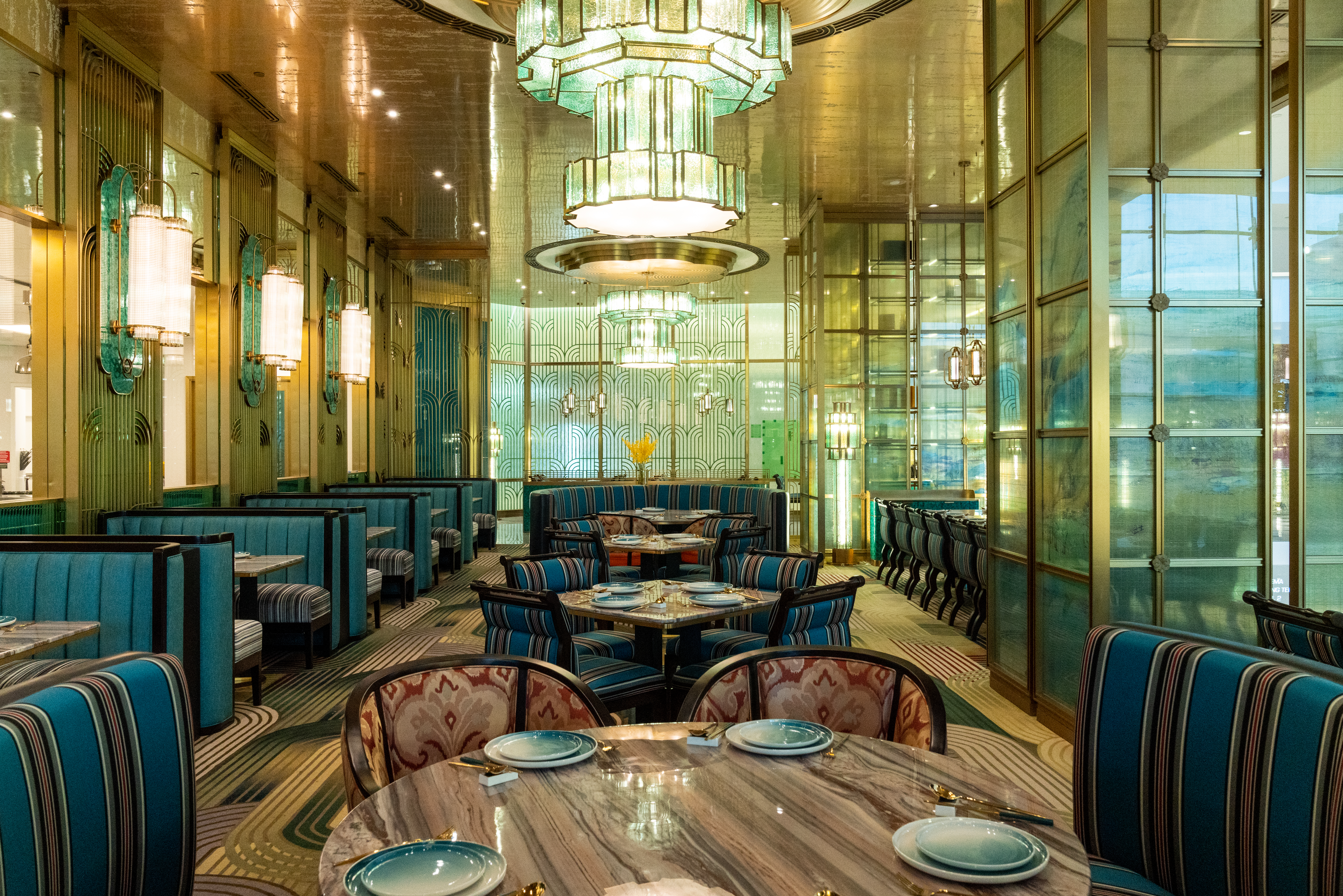 An opulent dining room with high ceilings, modern chandeliers, and blue booths.