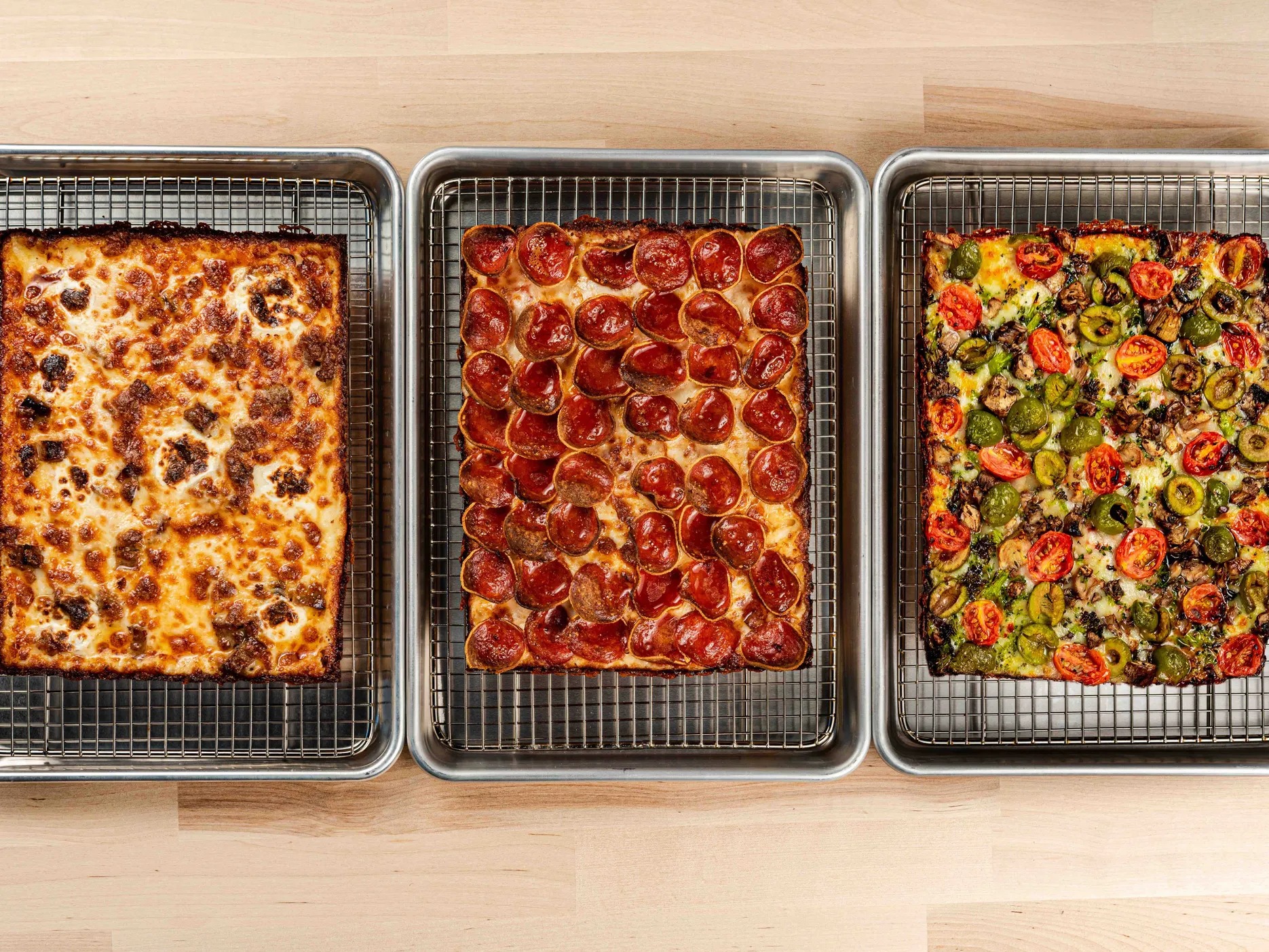 A trio of rectangular pizzas in pans.