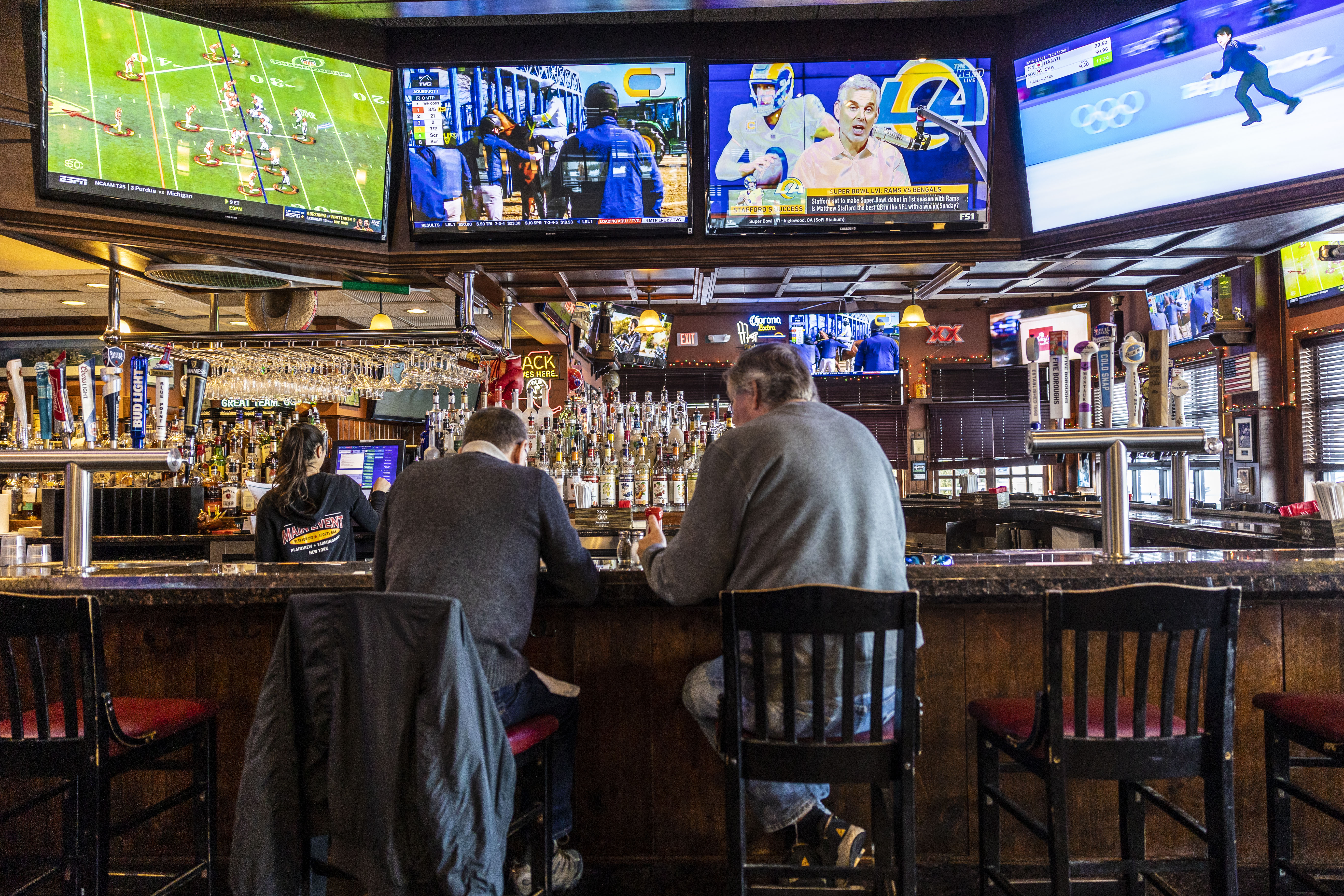 Two patrons sit at a Long Island bar/restaurant that features several screens showing different sports.