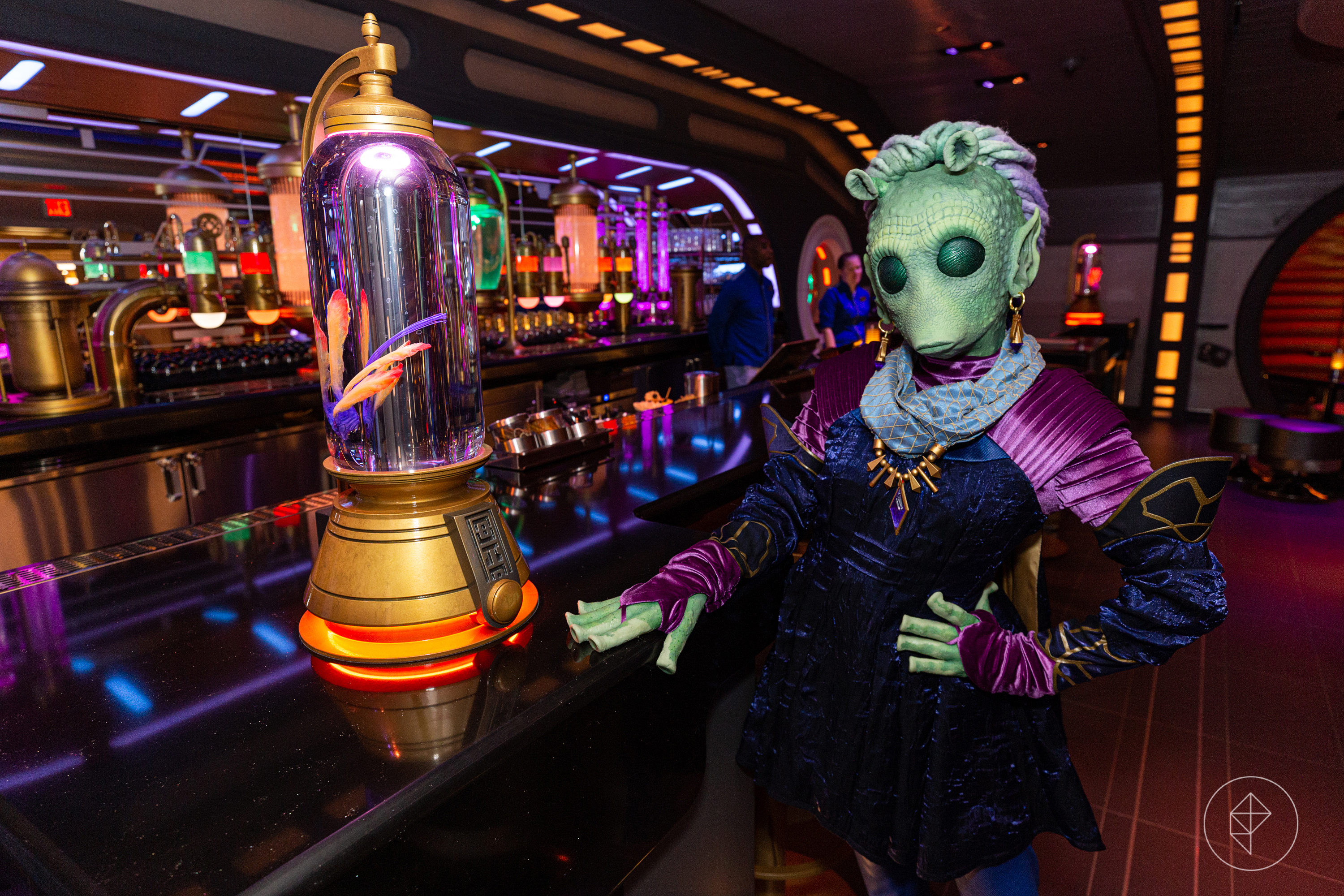 A woman in a green alien costume poses by a lavish bar, trimmed in gold and neon.