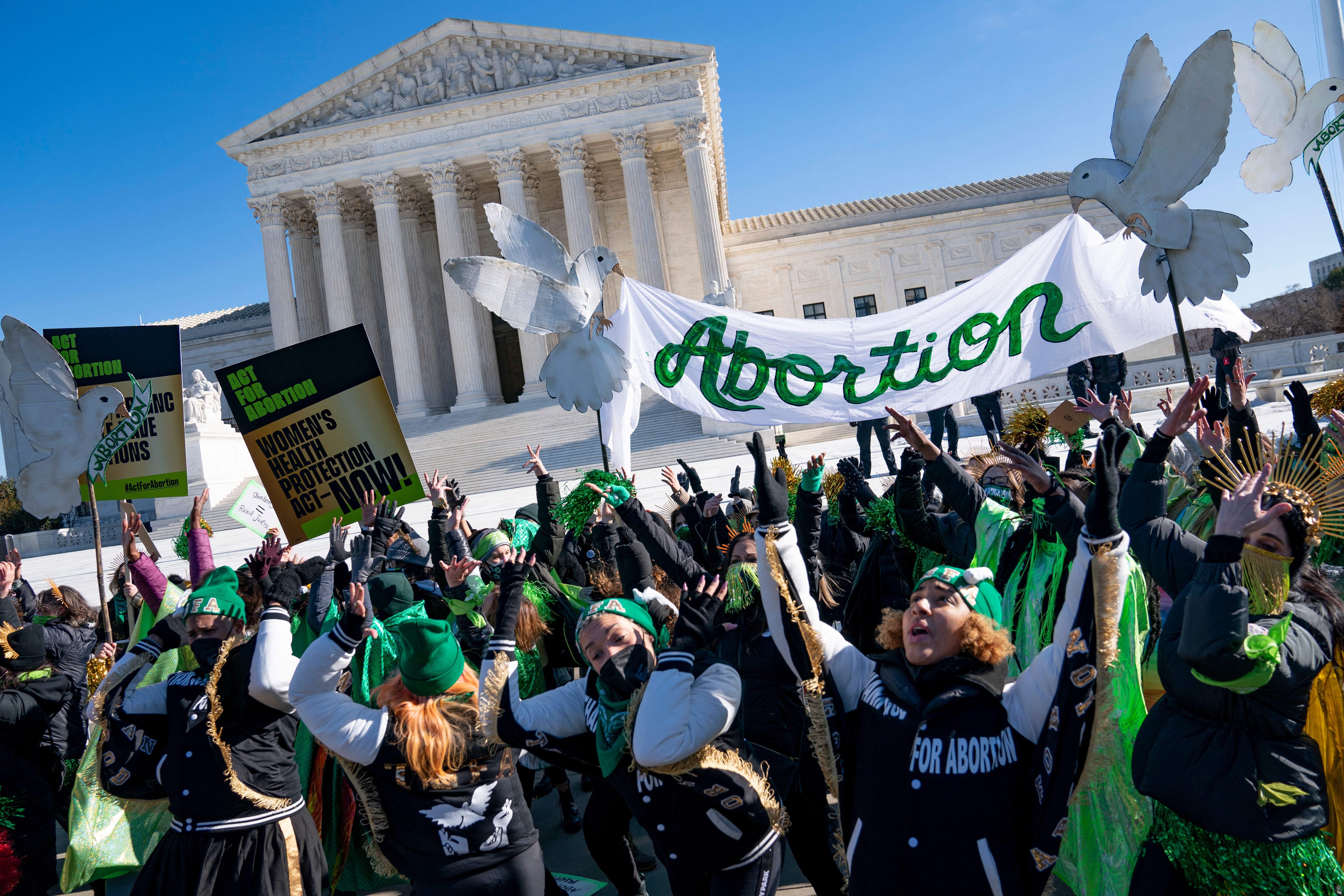 Demonstrators wearing green hold up a banner that reads “Abortion” in front of the Supreme Court building.