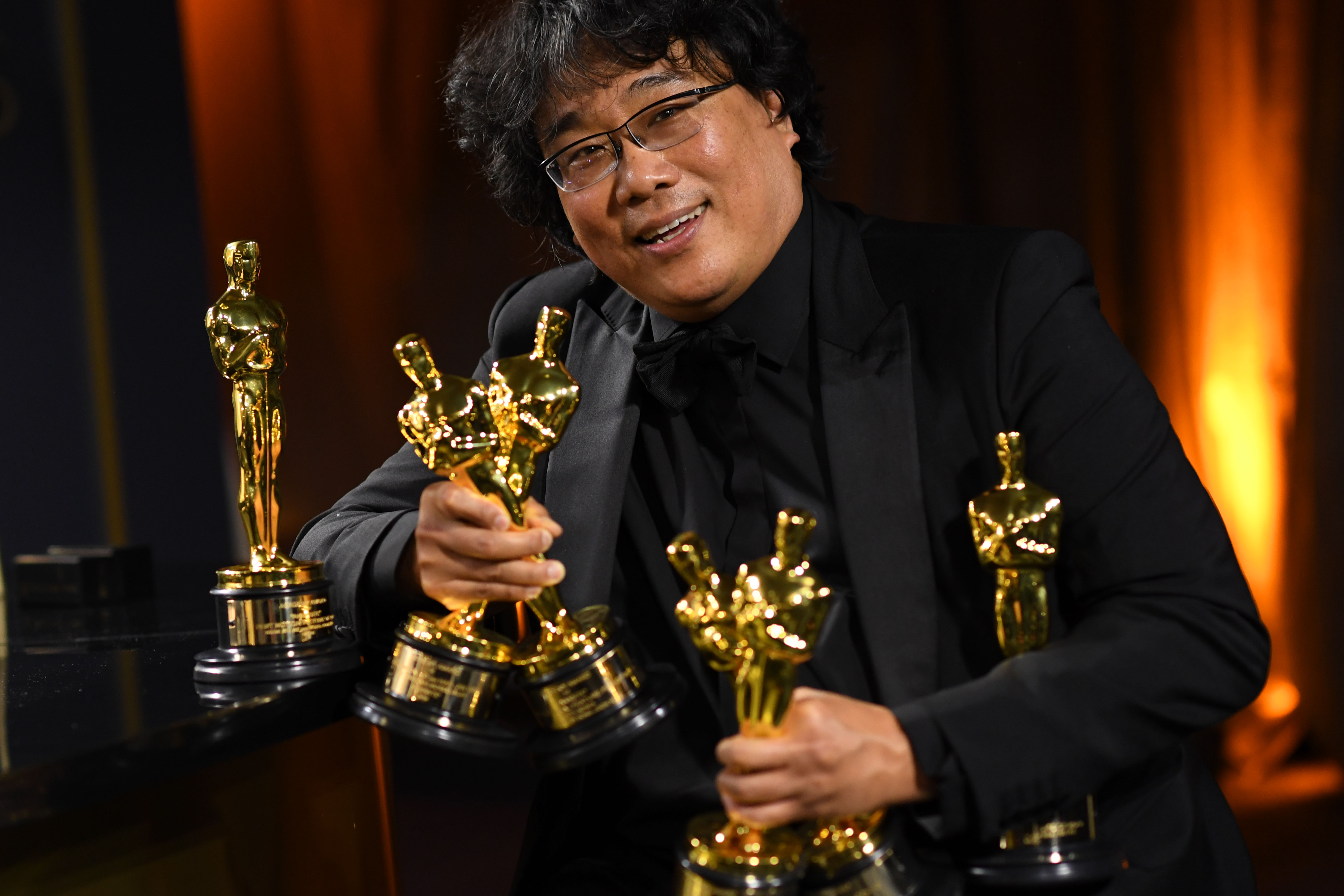 Bong Joon Ho holds several Oscars and smiles.
