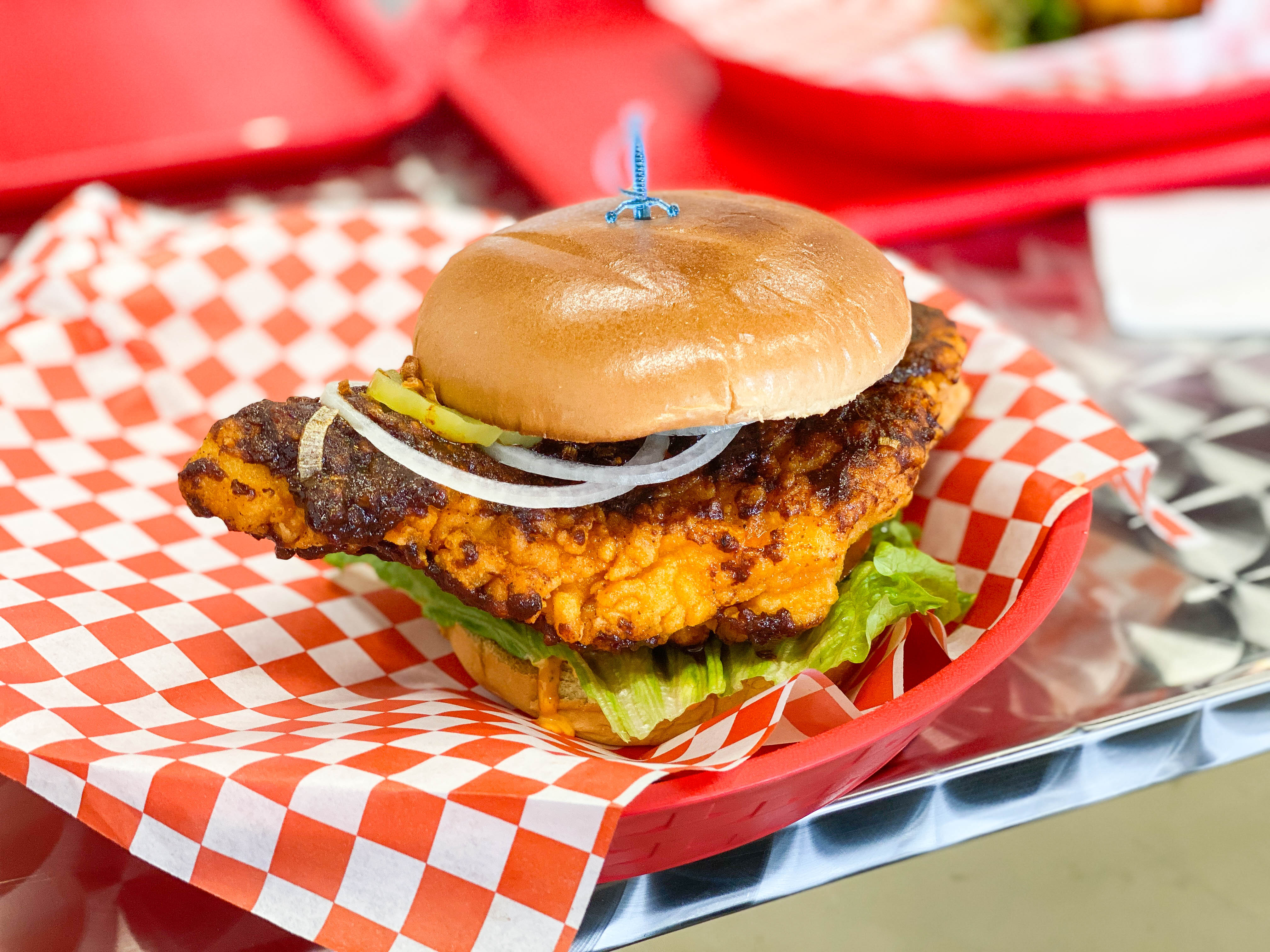 A fried chicken sandwich on red checkered paper at daytime.