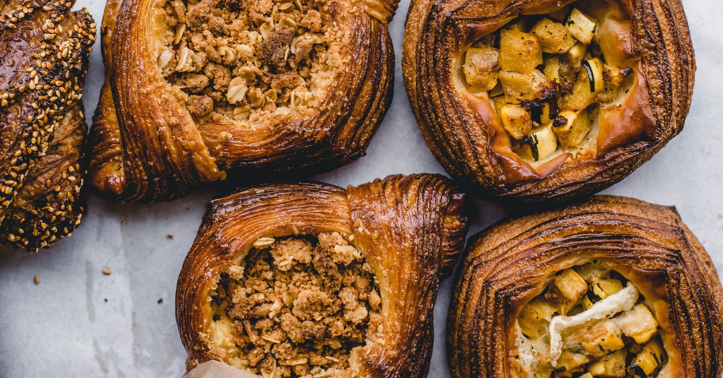 Several flaky pastries sit on a light surface, two filled with toasted oat crumble and two with small chunks of roasted squash.