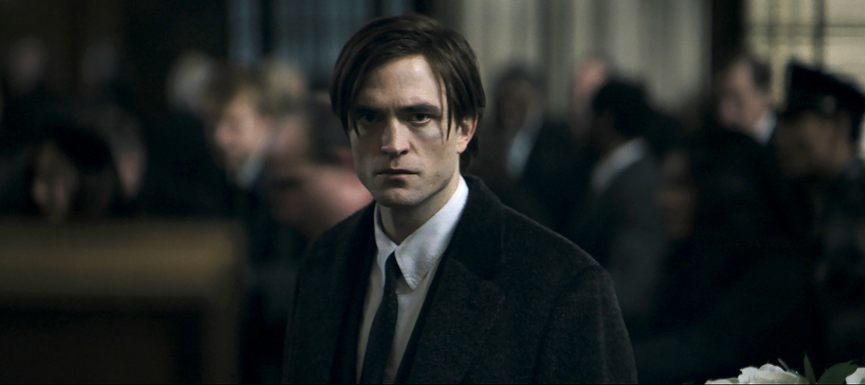 Robert Pattinson’s Bruce Wayne stares sullenly at the camera in The Batman. He’s wearing a formal suit and has a terrible haircut.