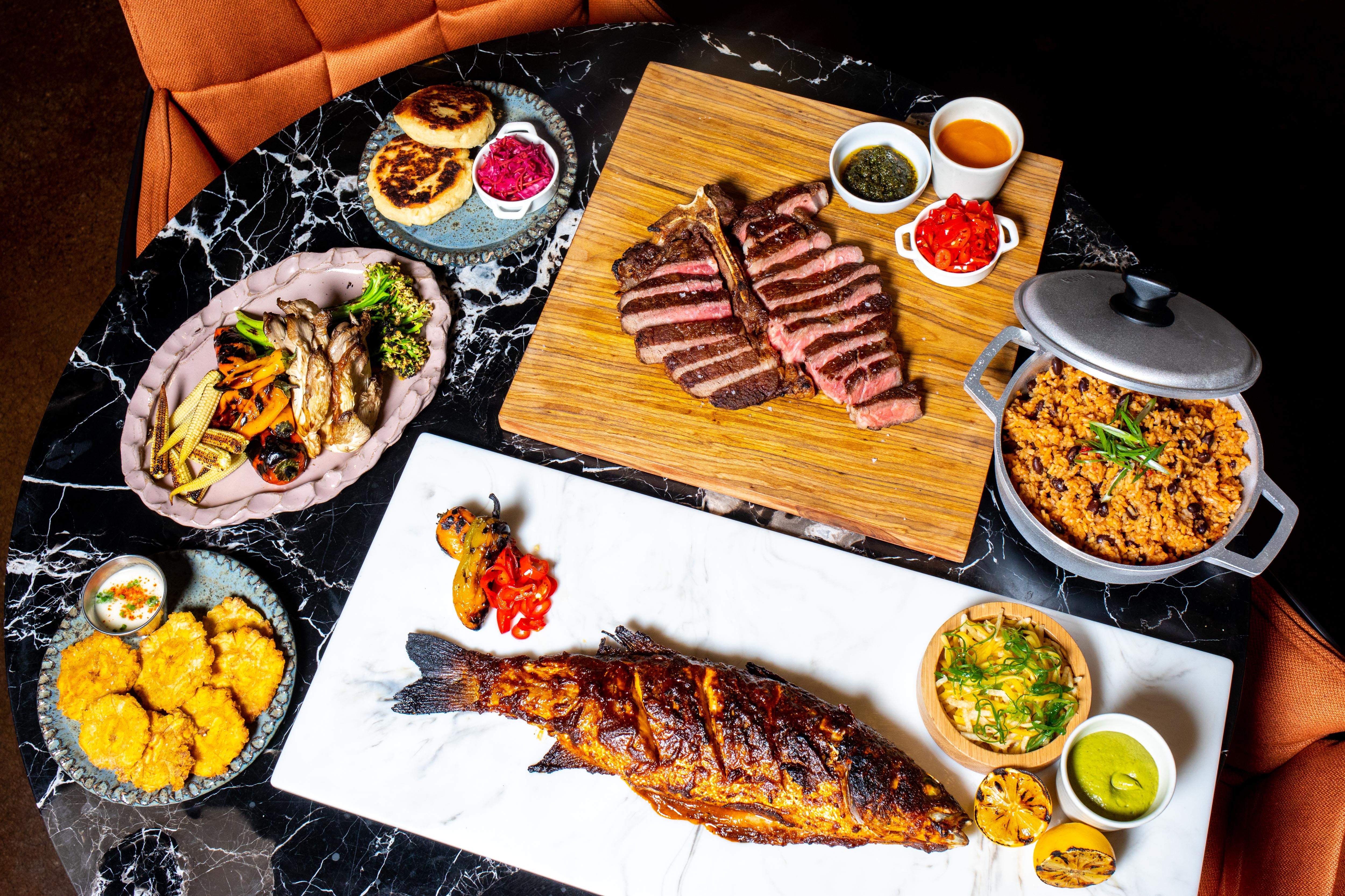 A huge spread of fish, sliced steak, dips, and sides on a black marble table