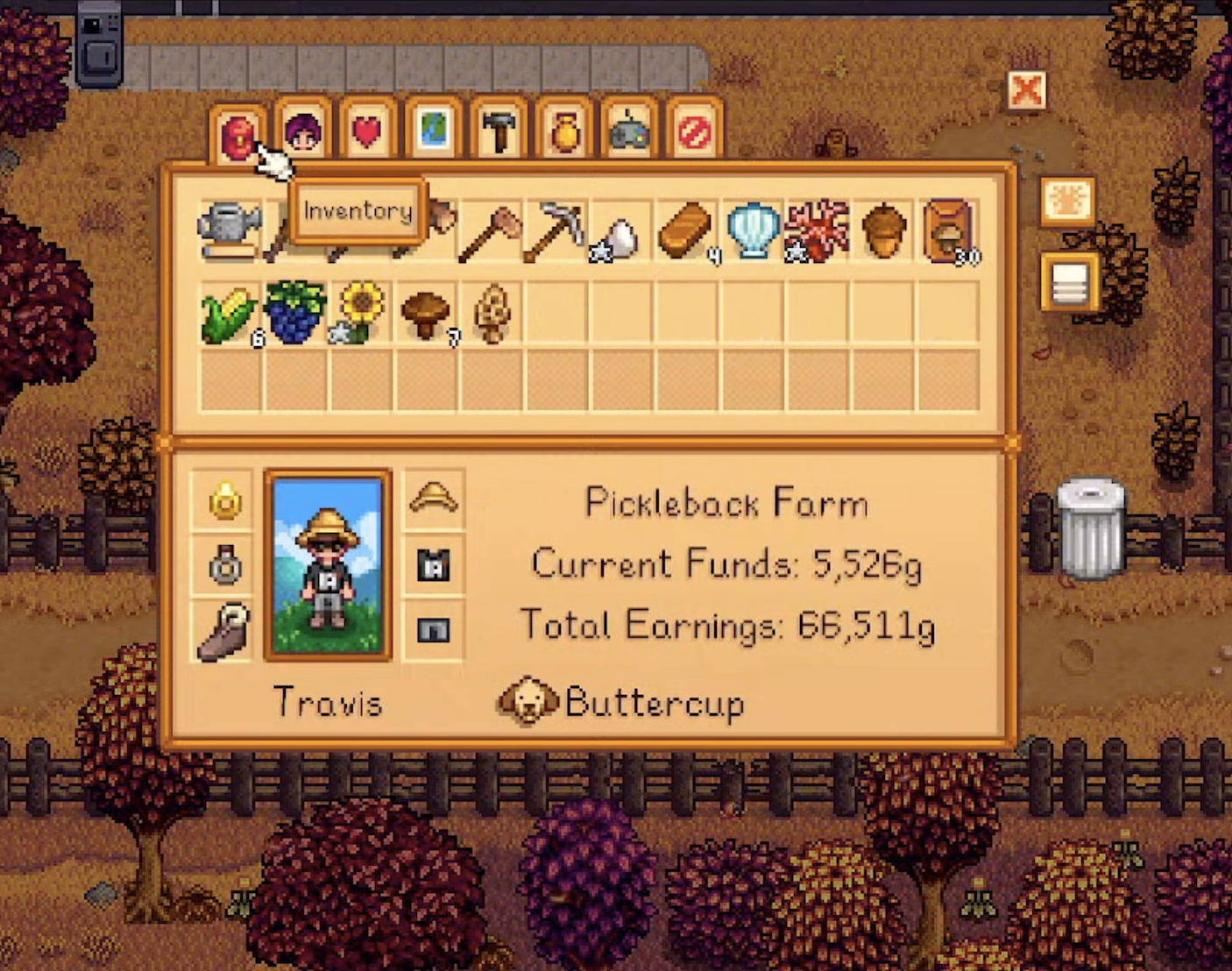 The menu for the game Stardew Valley. There are 8 tabs up top, and Travis’ inventory is displayed below them. At the bottom left we see a depiction of Travis’ character, named Travis, and on the right is the text “Pickleback Farm current earnings 5,526g total earnings 66,511g”. At the very bottom we see the face of a yellow dog named Buttercup. Behind the menu are autumn trees and leaves.