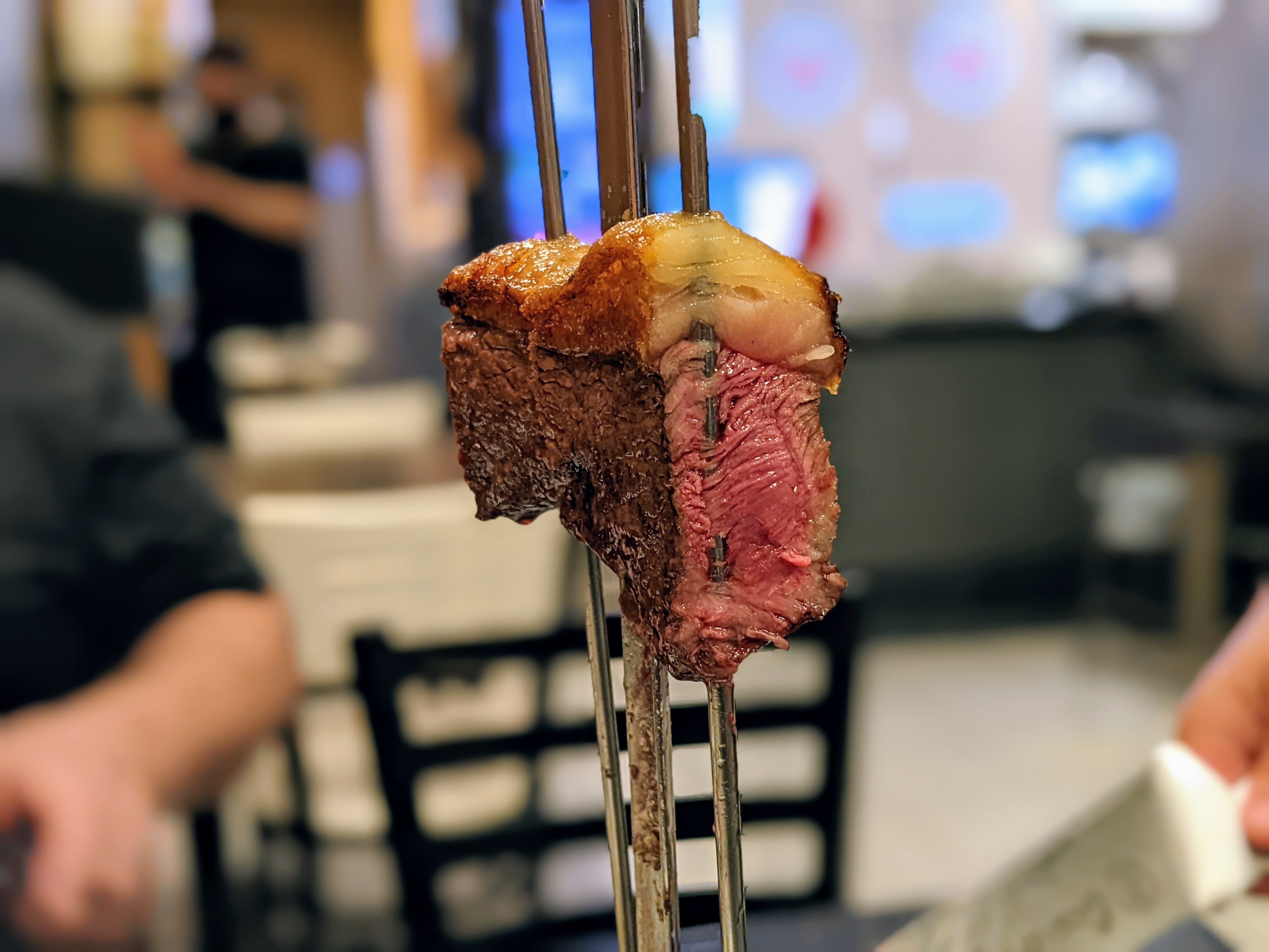 A cut of steak on a skewer with the fat cap still attached.