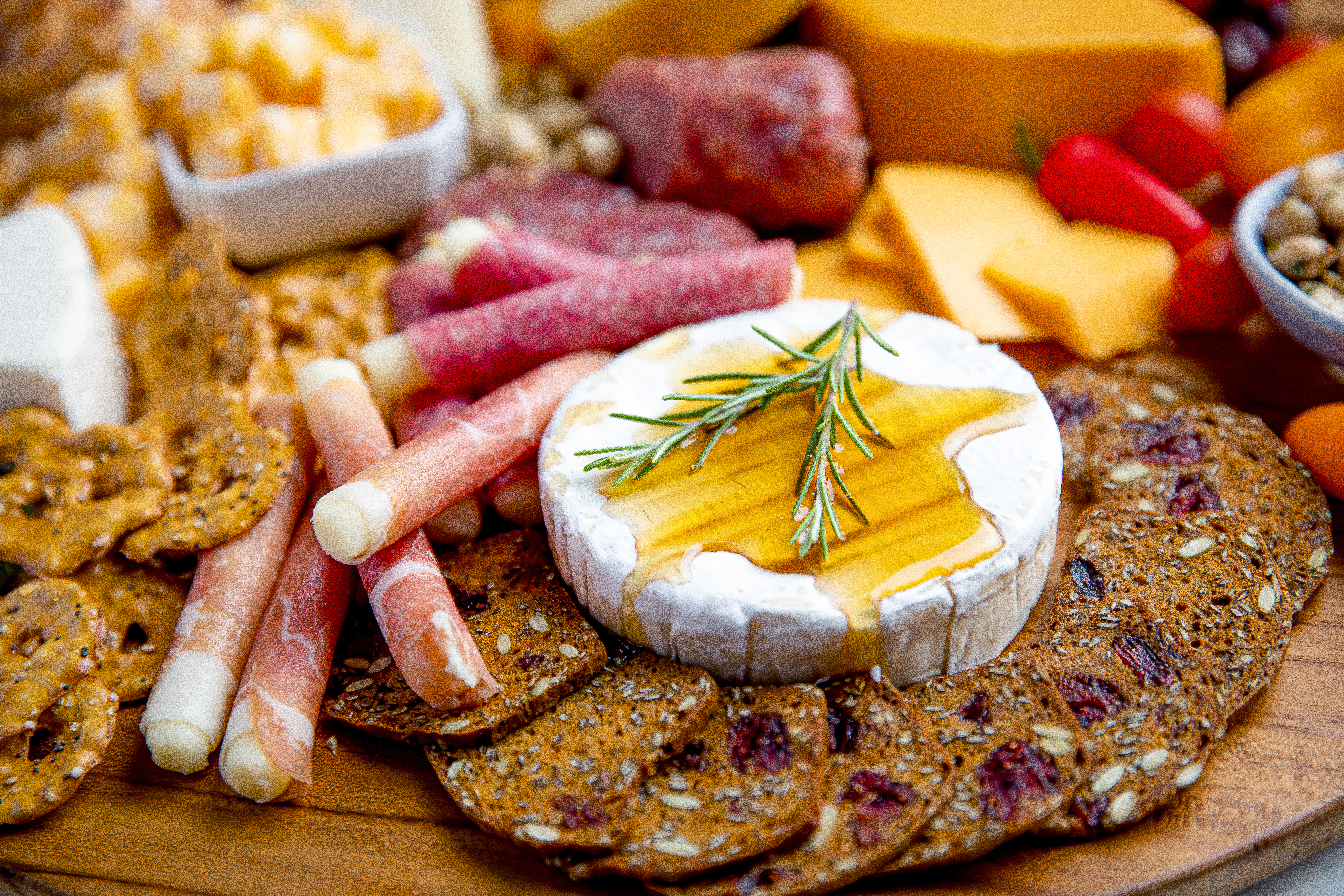 A board with sliced and rolled meats and a round of cheese with honey.
