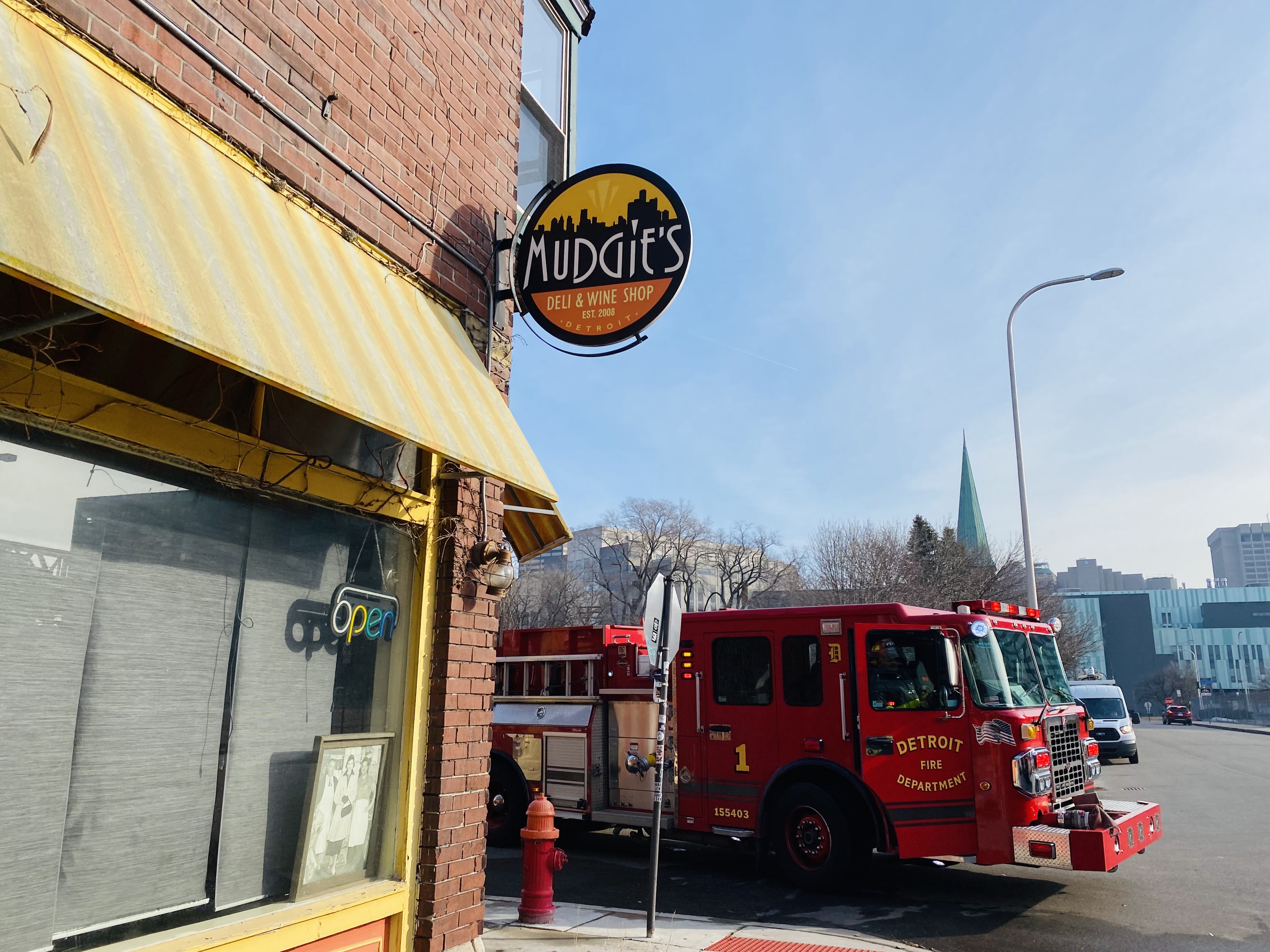 A red fire truck parked next to a stop sign at the corner of Porter and Brooklyn in Detroit. Yellow and white awning and sign that says Mudgie’s also pictured.