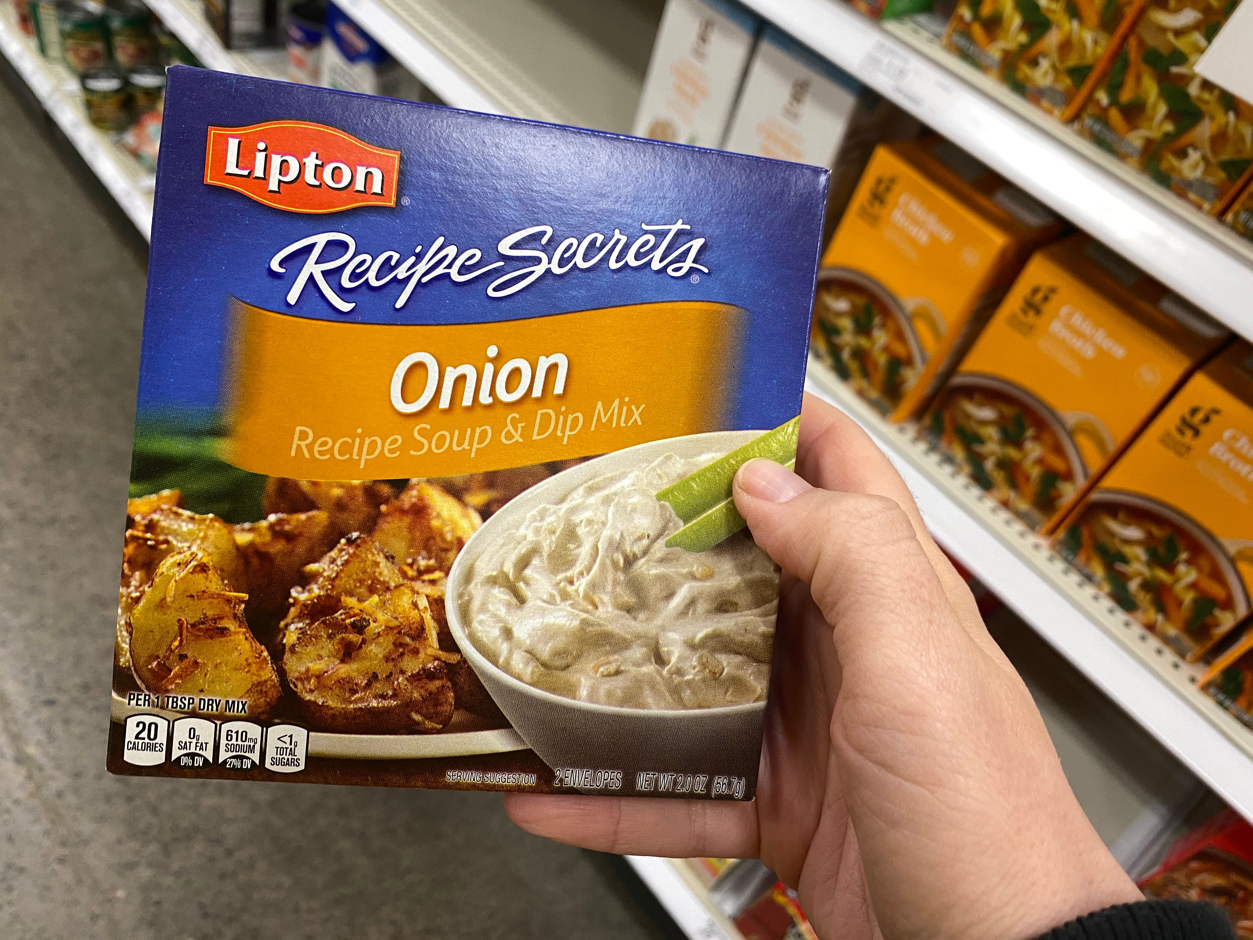 Hand holds up a box of Lipton onion soup mix in a grocery aisle.