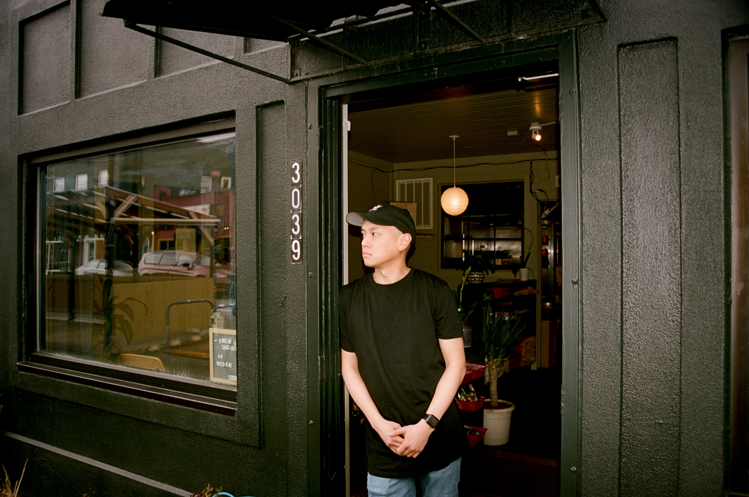 Jimmy Le, wearing a black baseball cap and t-shirt, leans against the doorway at Thom