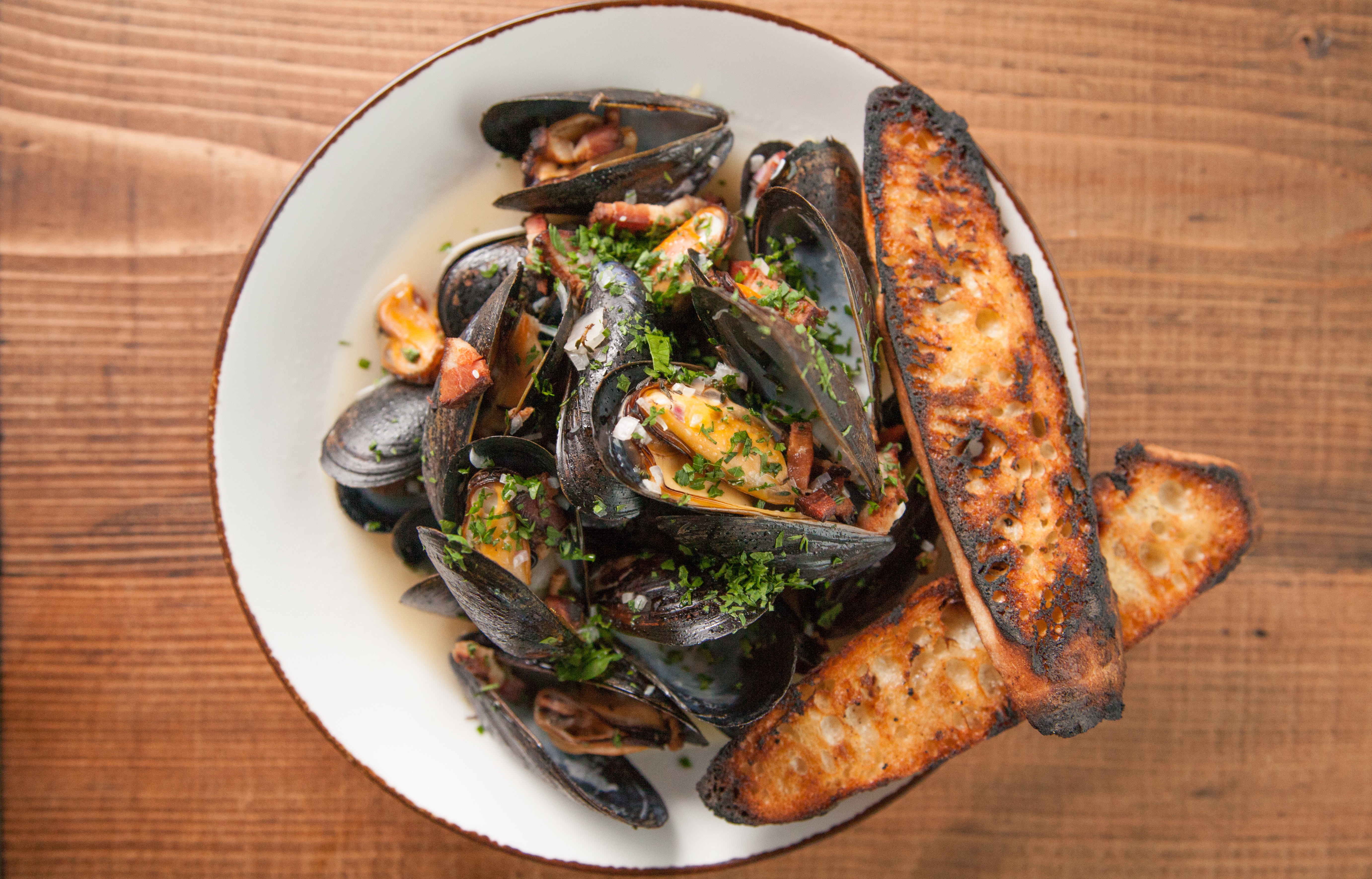 An overhead shot of a pile of steamed mussels in a bowl with grilled bread.