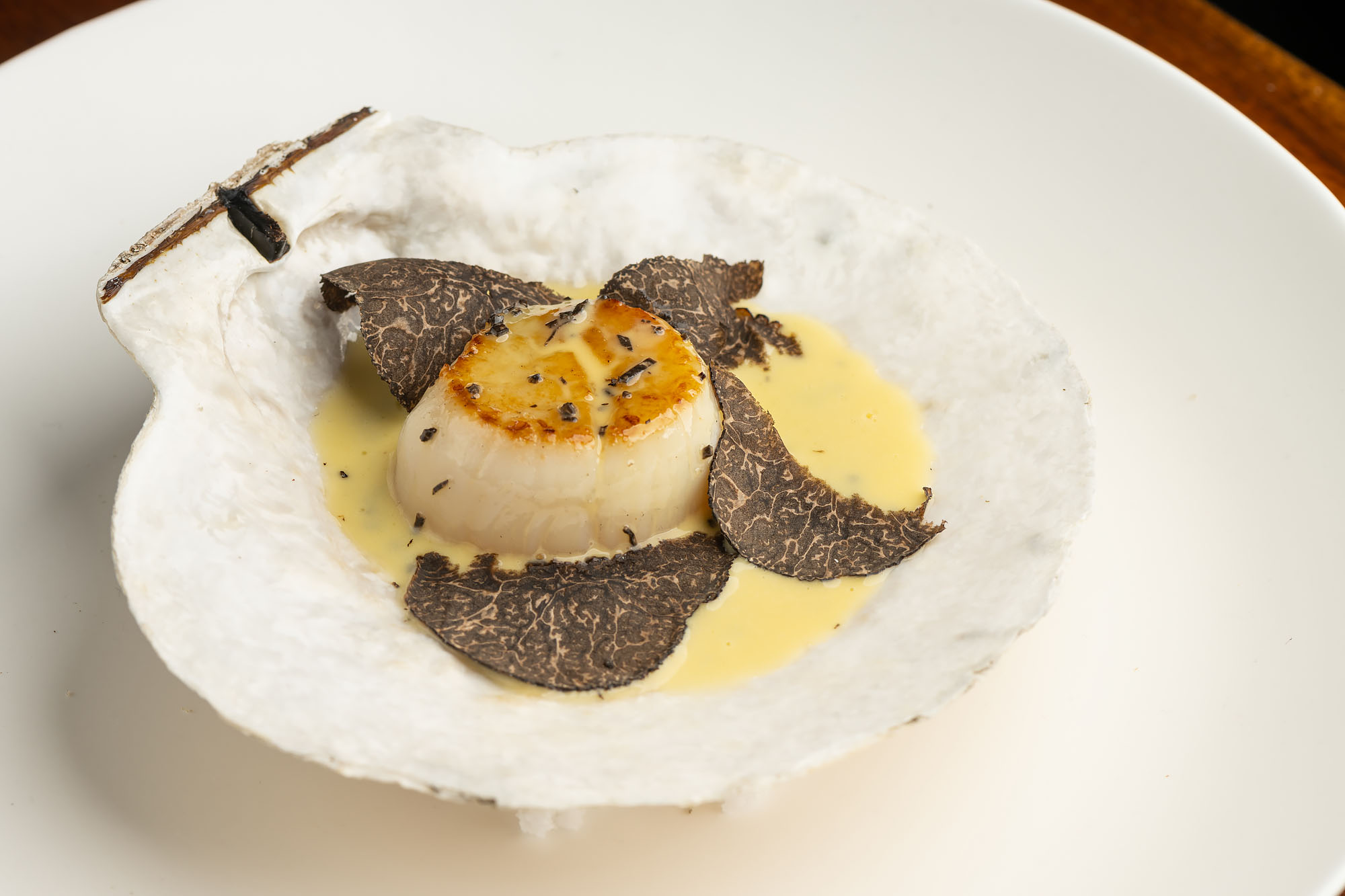 An abalone piece seared to brown with shaved truffle in a shell.