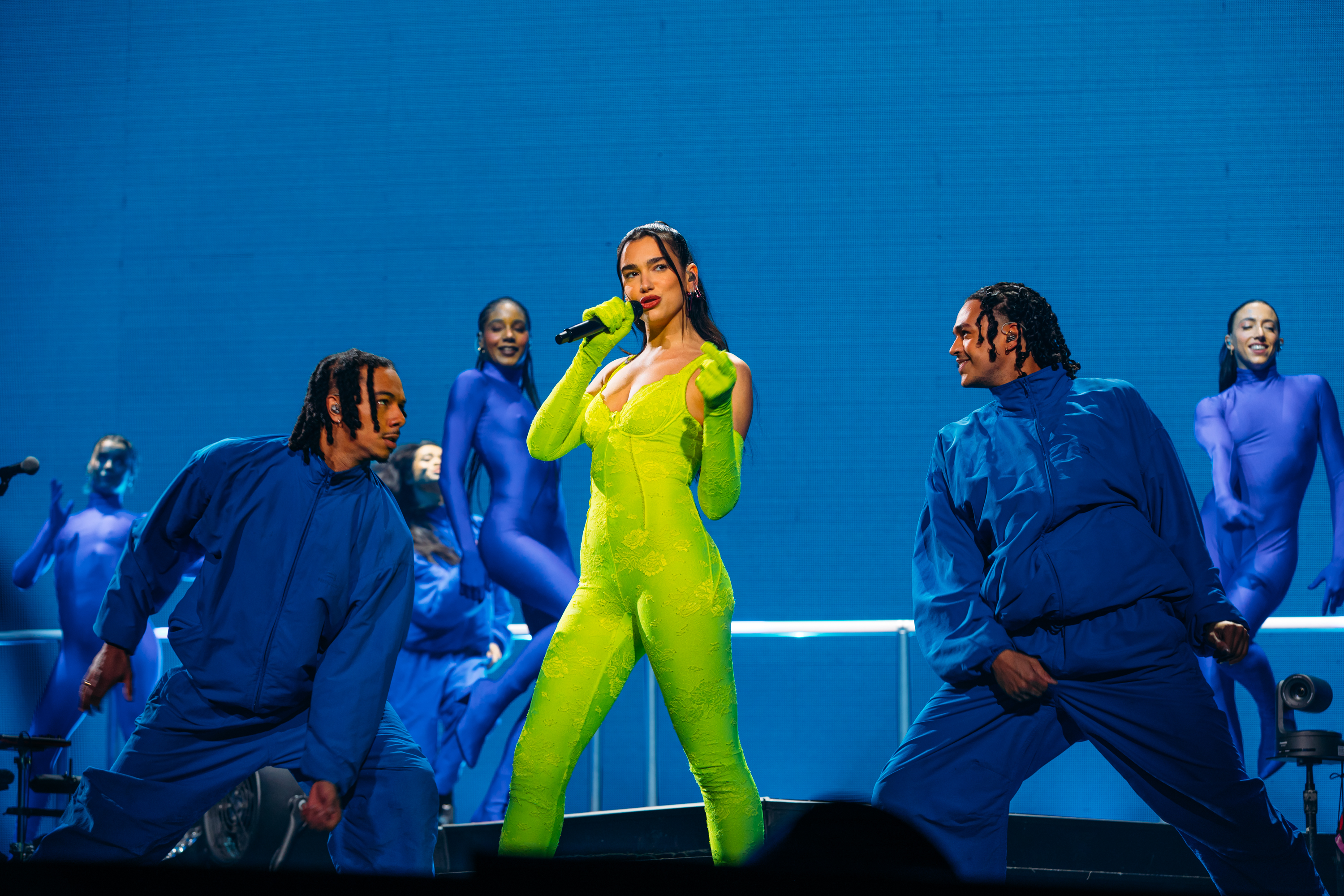 Dua Lipa stands in the middle of a stage in Chicago, dressed in a lime green leotard with a microphone in her hand.
