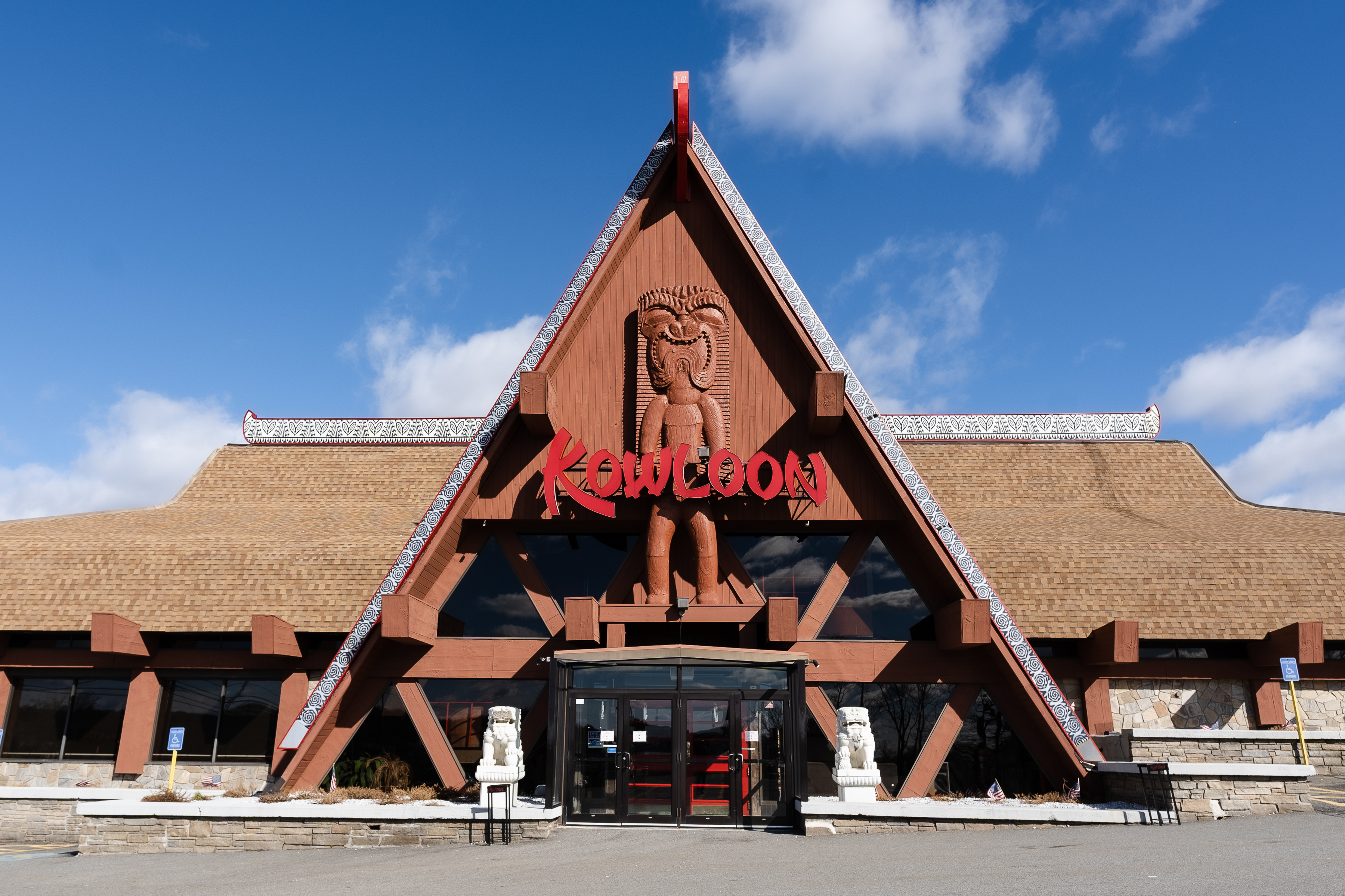 The exterior of Kowloon restaurant has a large triangle-shaped main entrance with a wooden totem on the facade.
