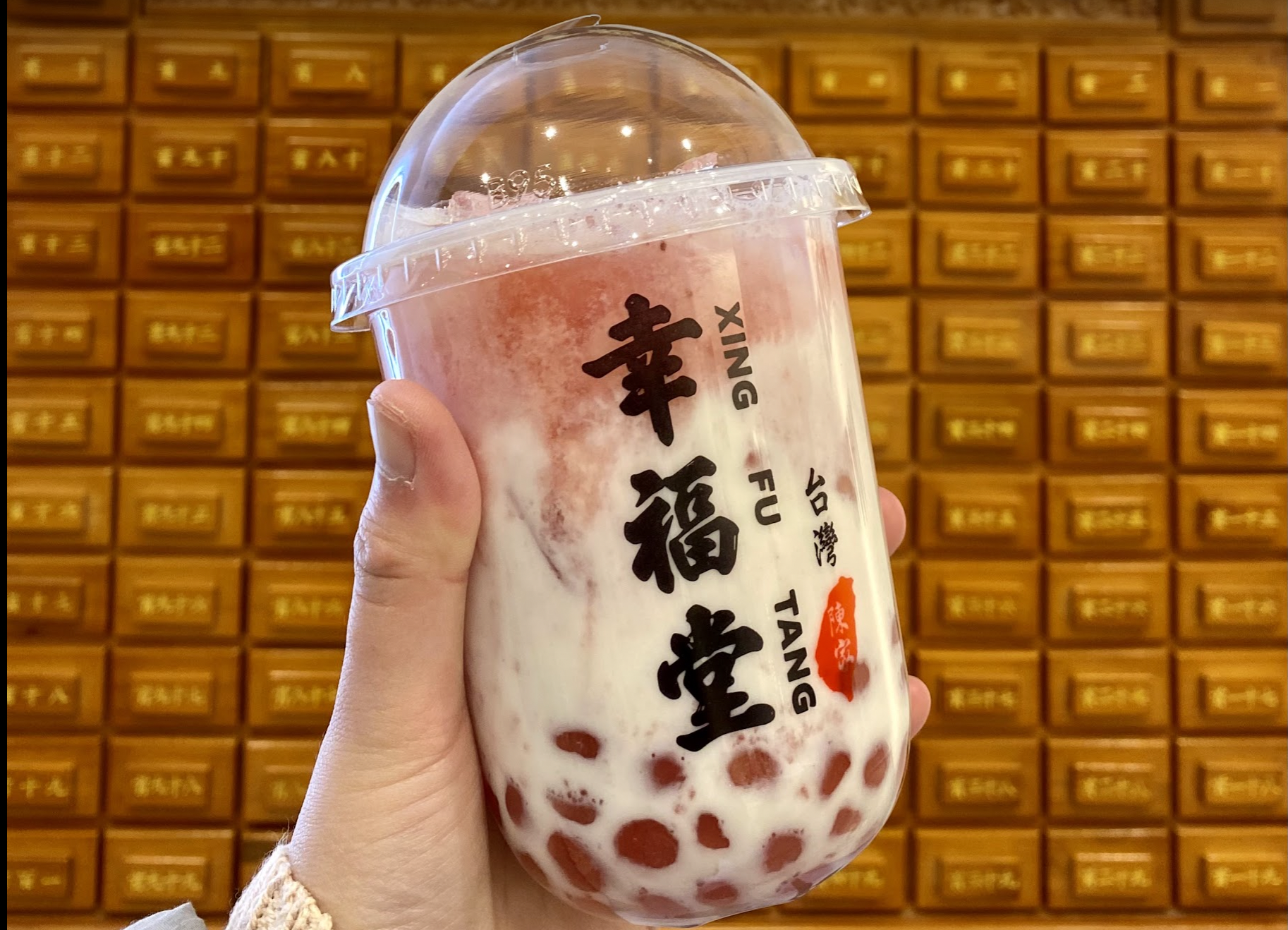 A white and pink bubble tea is held up by a hand.