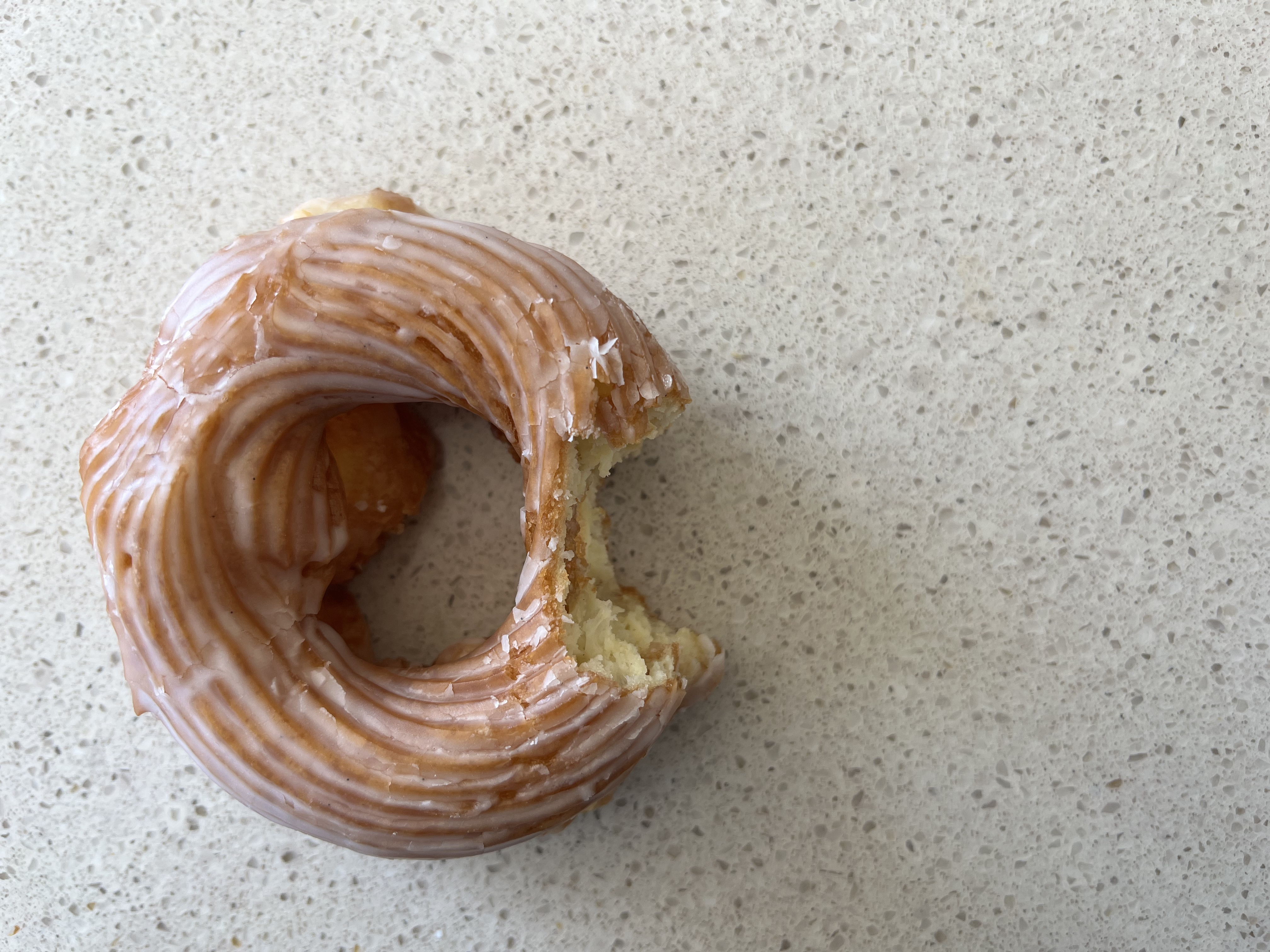 A glazed cruller with a visible bite mark sits above a marble countertop