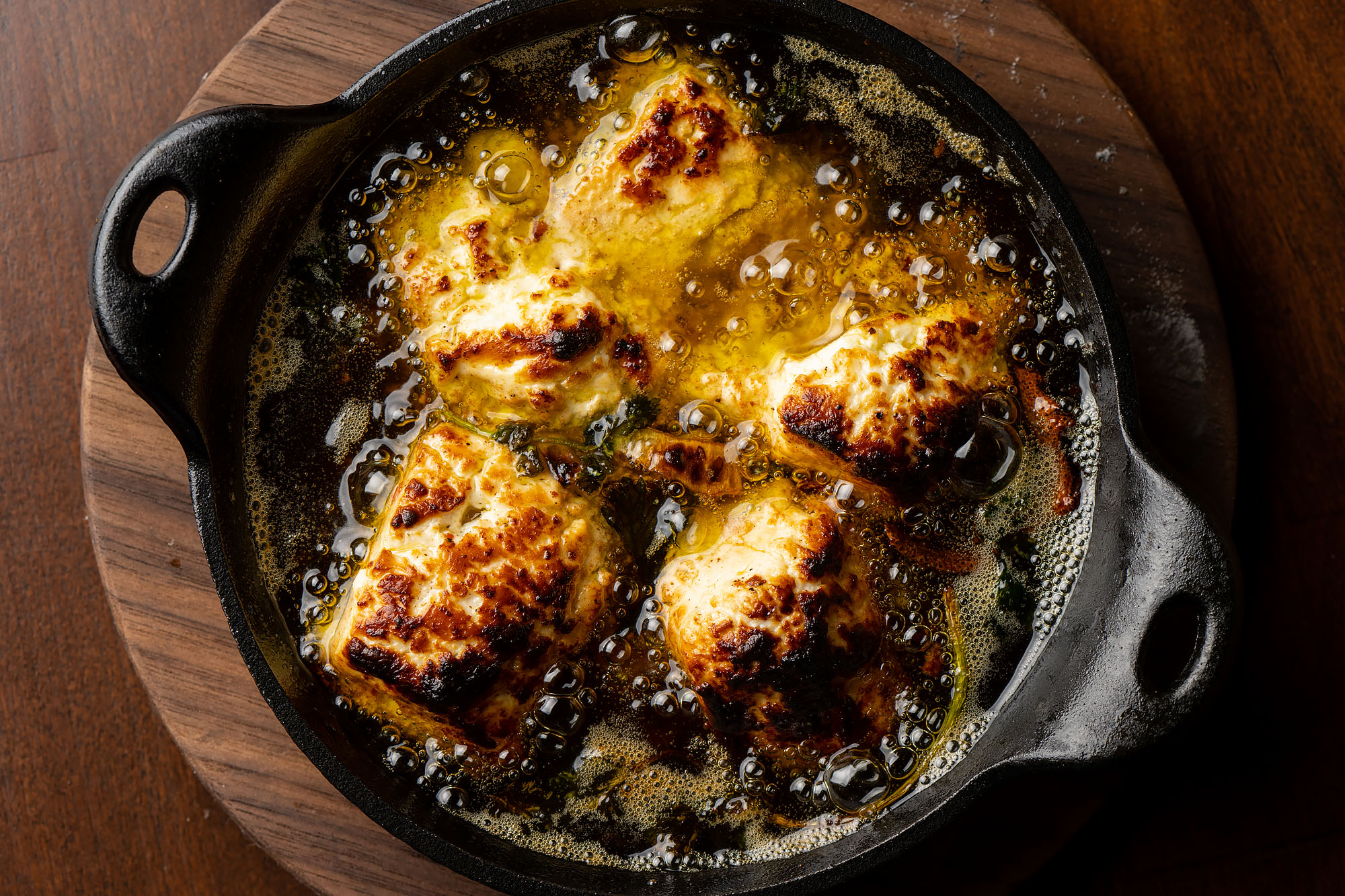 An overhead shot of boiling oil in a cast iron pan with squares of blistered cheese.