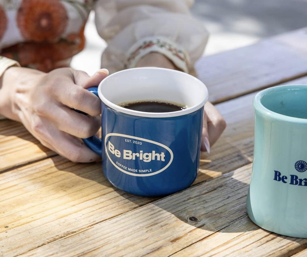 A dark blue coffee mug with black coffee held by two hands.